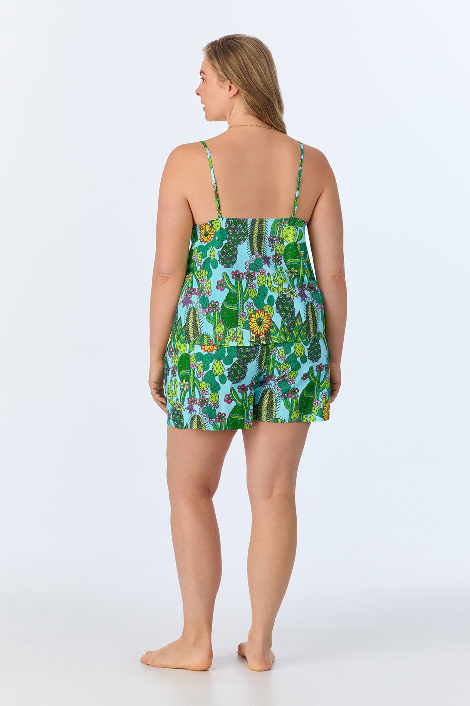 A woman stands barefoot facing away, wearing the Cami Shorty PJ Set - Cactus Poplin, a colorful sleeveless pajama set with a green and blue botanical cactus print. The background is plain white.
