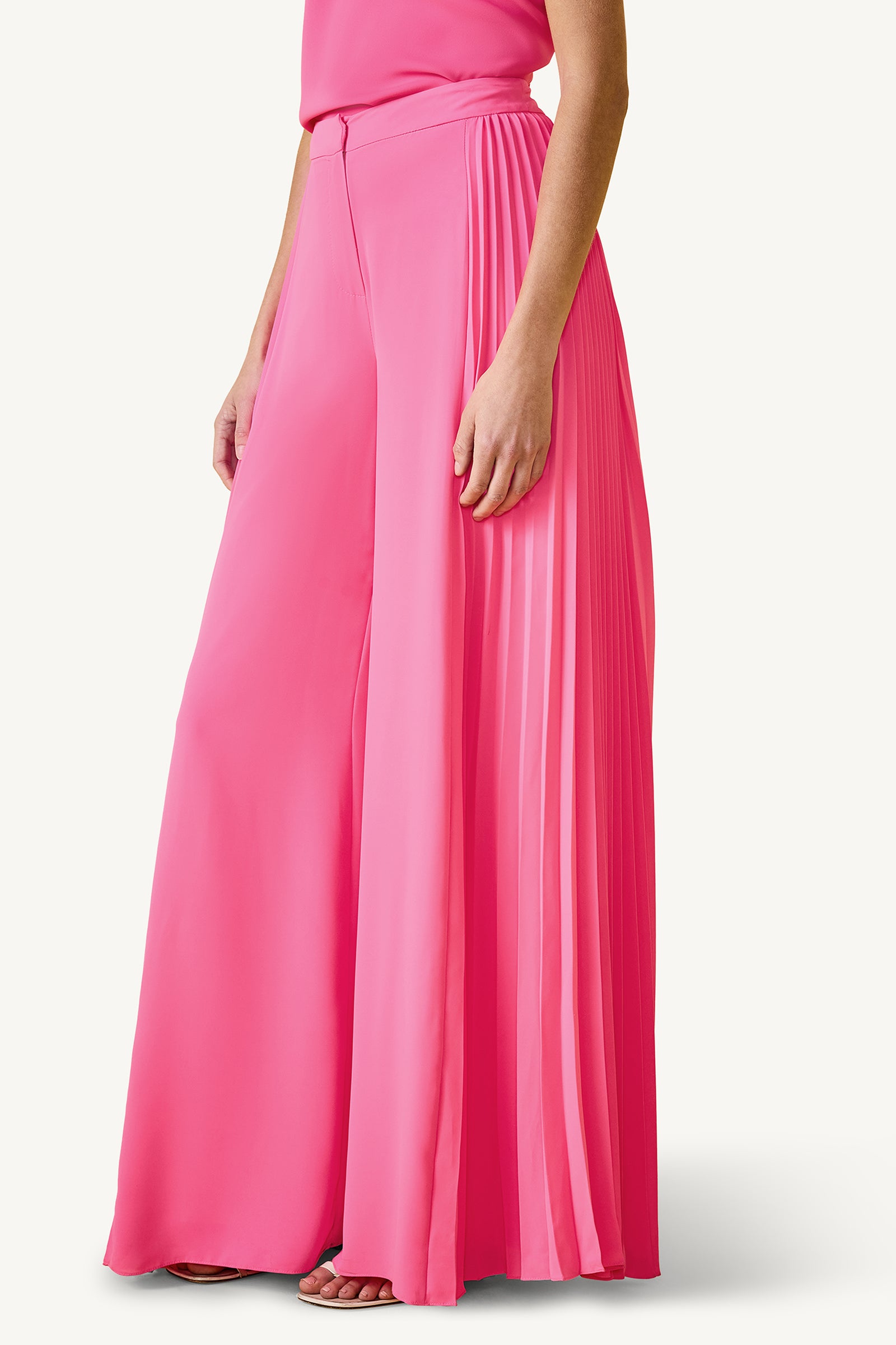A woman’s lower body is shown against a plain background, wearing the Frame Wide-Leg Pleated Pant - GS Georgette in bright pink, styled with a matching top and open-toe shoes. One side features pleated detailing for added style.