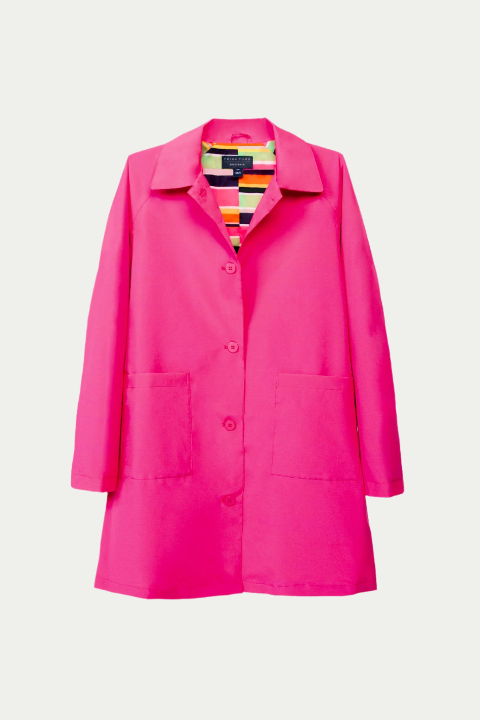 The TT X SR Mac Rain Coat - Pink is a bright pink button-up coat with two large front pockets, a collar, and a colorful striped inner lining, shown on a white background.