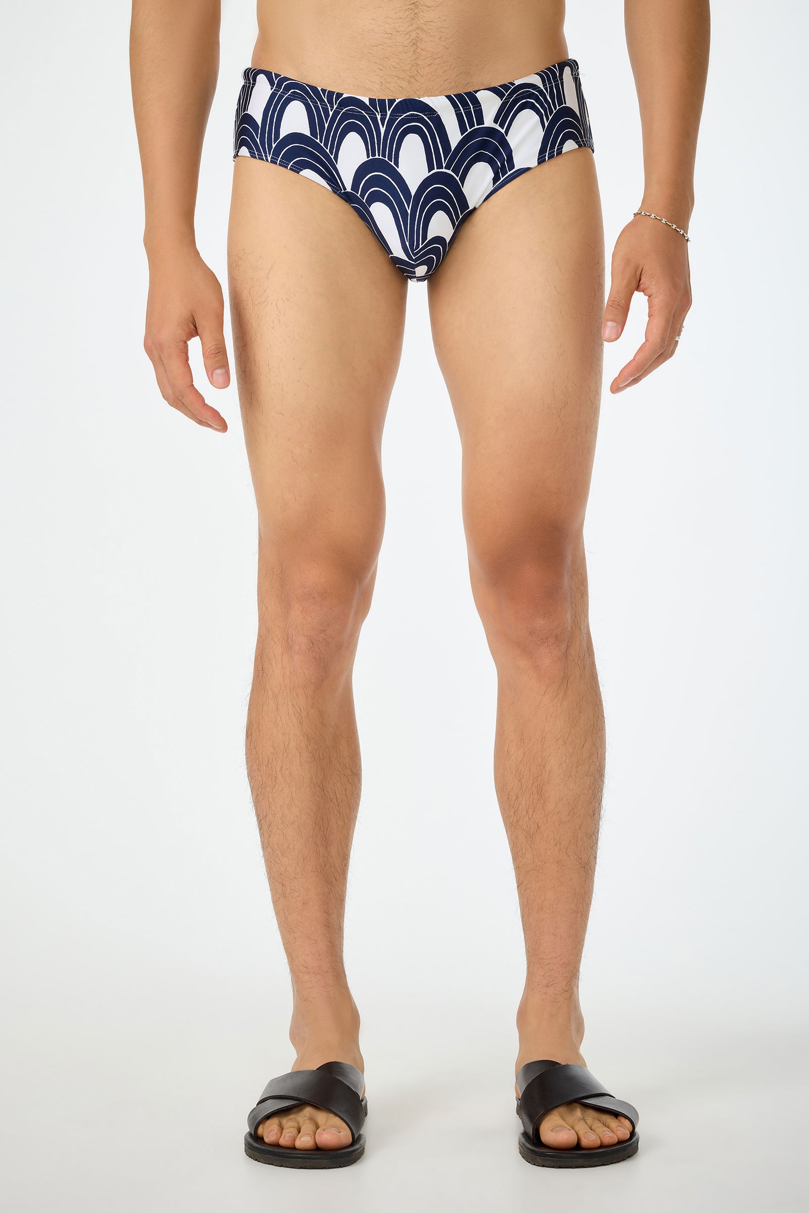 A person is shown against a white background, wearing the Bondi Swim Brief - Arches in Arches Swim color with black sandals. The photo is cropped at the neck, highlighting the swimwear and lower body.