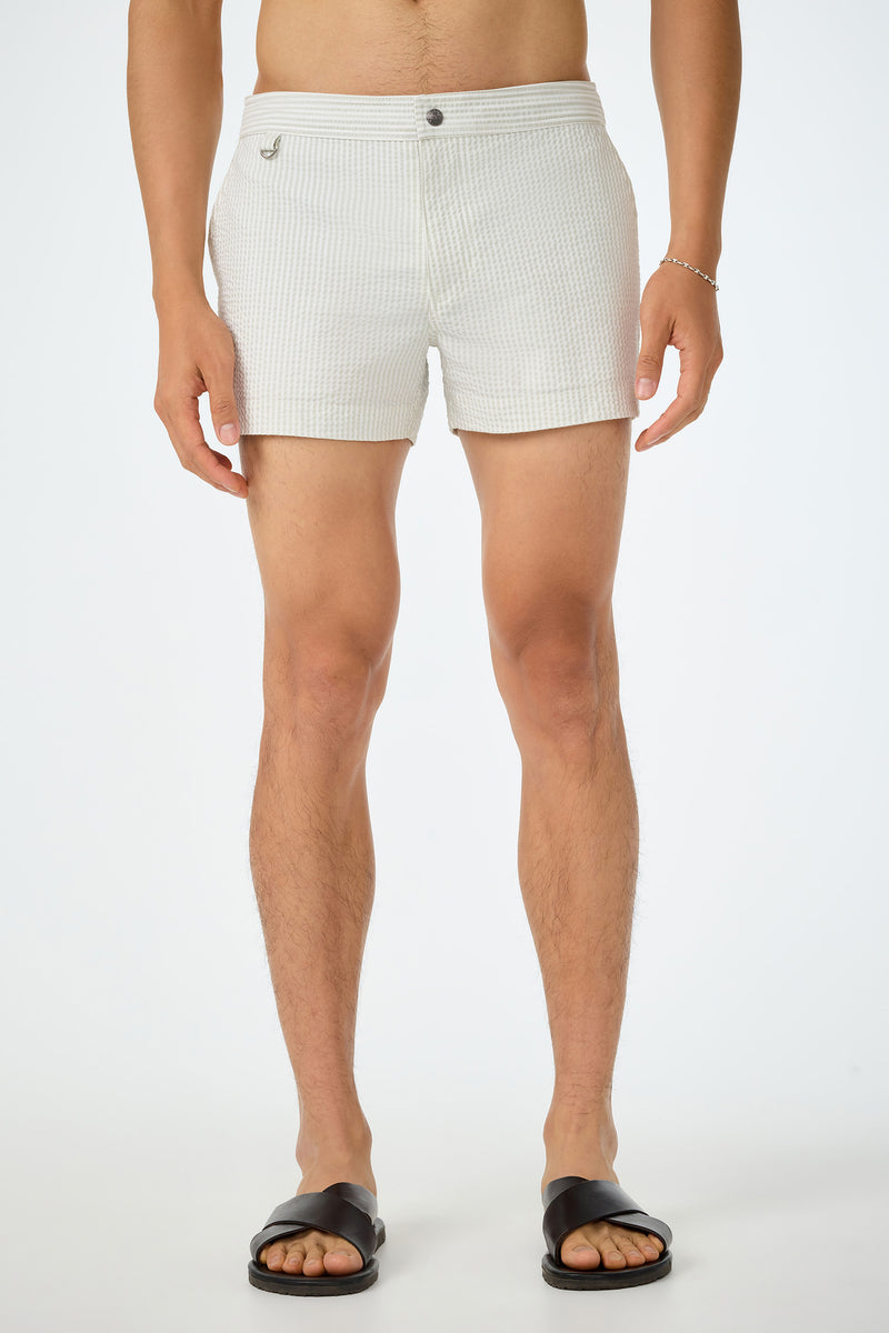 A man wearing the Chico Swim Trunk - Seersucker in Sand and black sandals stands against a plain white background. His upper body is not visible.