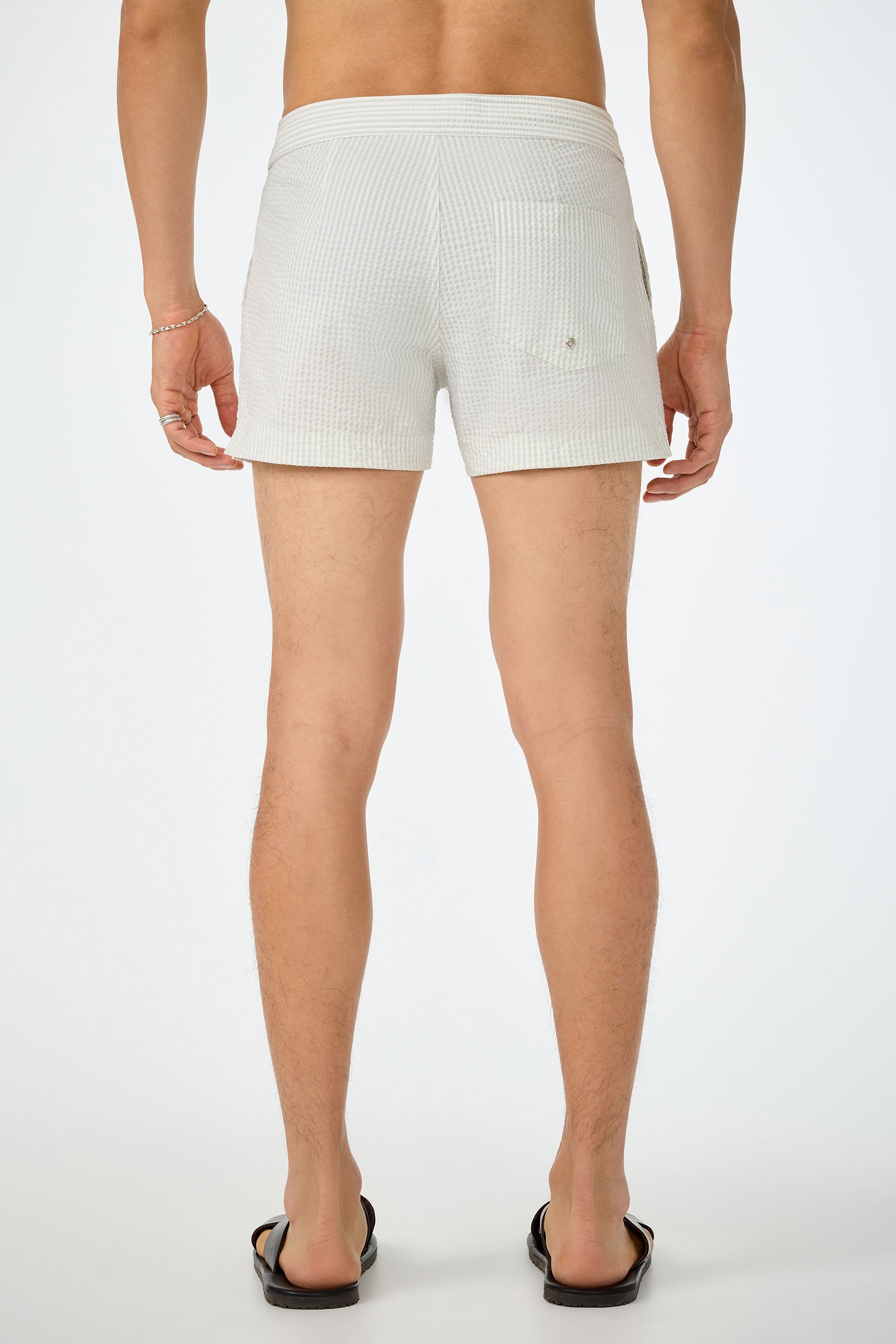 A person faces away from the camera, wearing Chico Swim Trunk - Seersucker with a back pocket and black flip-flops against a plain white background.