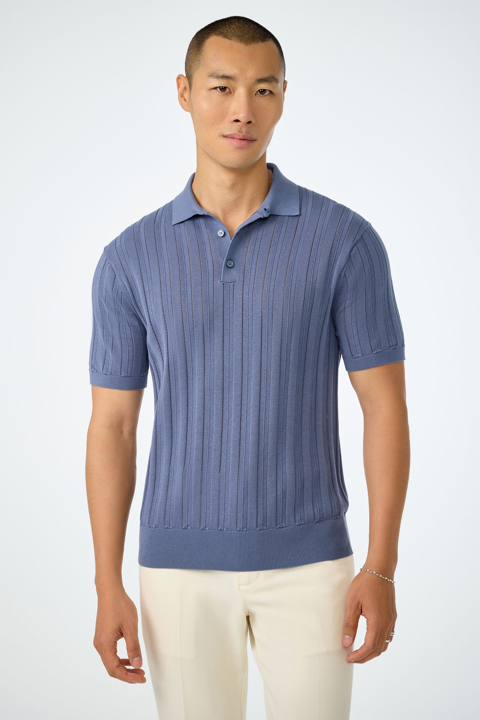 A man in a blue Kensington Short-Sleeve Polo and off-white pants stands against a plain light background.