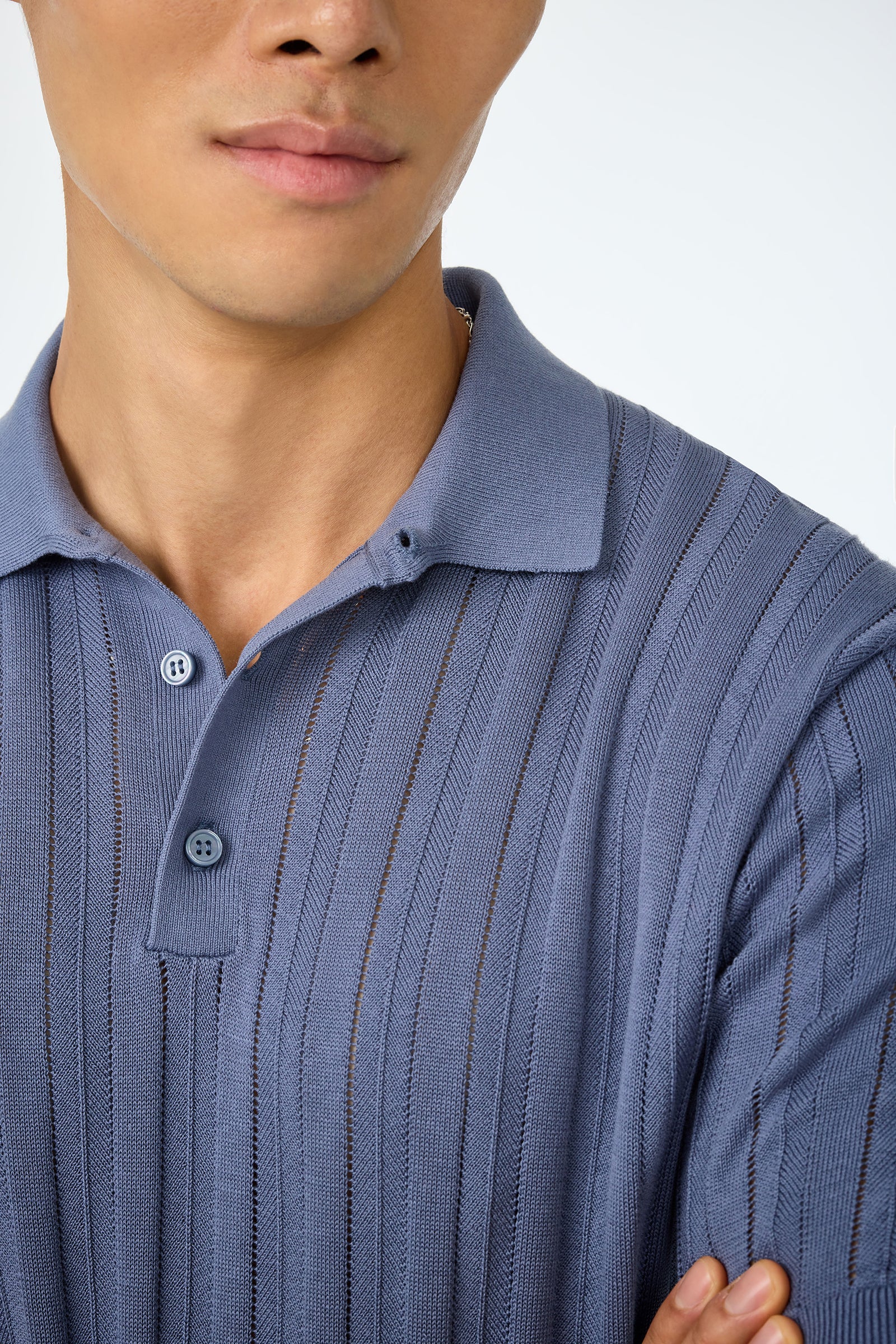A close-up of a person wearing the Kensington Short-Sleeve Polo in light blue with vertical textured stripes, highlighting the collar, buttons, and part of their face and upper body against a plain background.