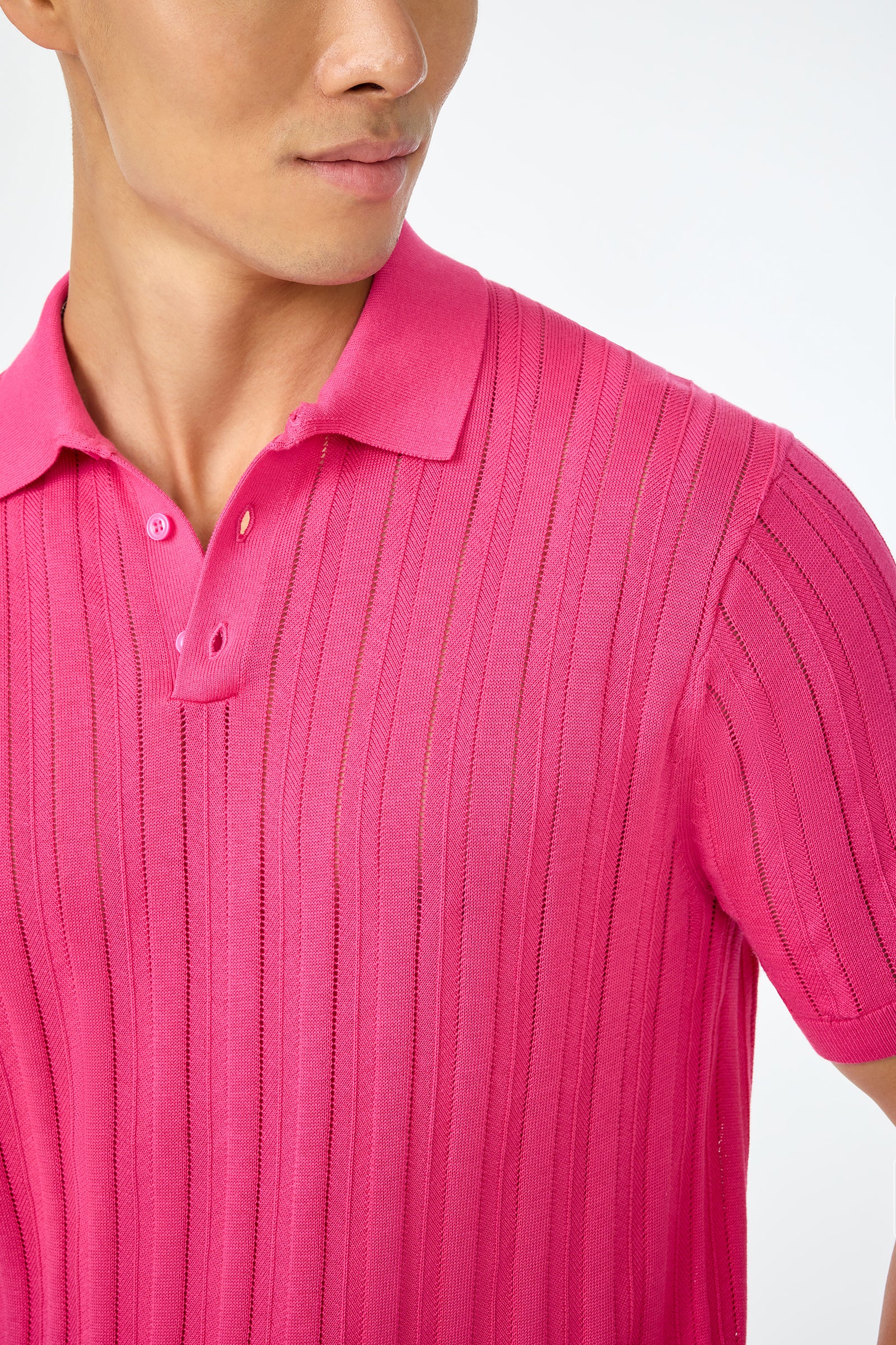 A person wears the Kensington Short-Sleeve Polo in bright pink, featuring a ribbed texture, collar, and buttons. The image is cropped to show the lower face, neck, and upper torso against a plain light background.