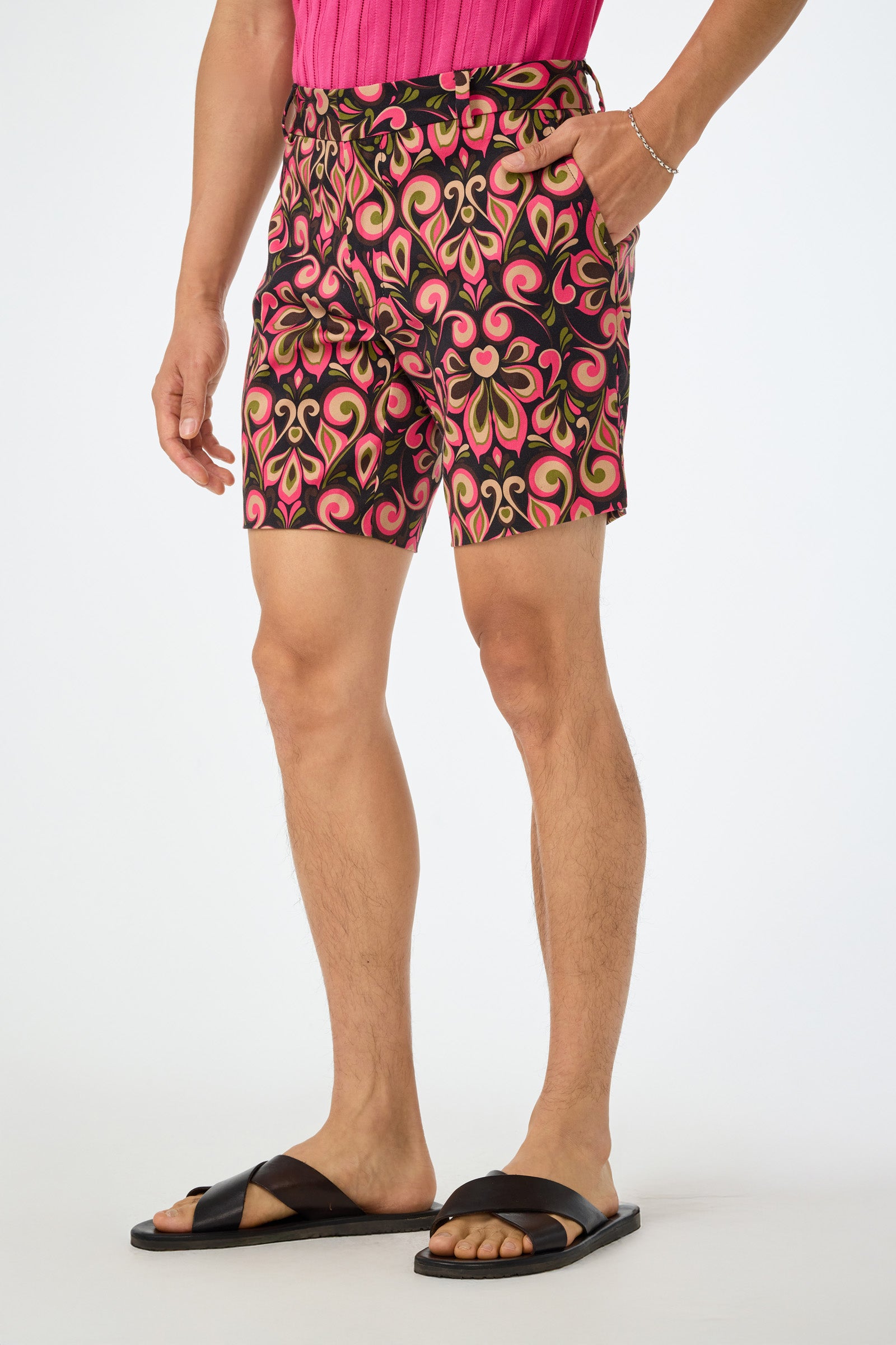 Wearing black sandals, a person models the Lawrence Short - Sanctuary Herringbone, featuring colorful pink, yellow, and black patterns, standing with one hand in their pocket against a plain white background.