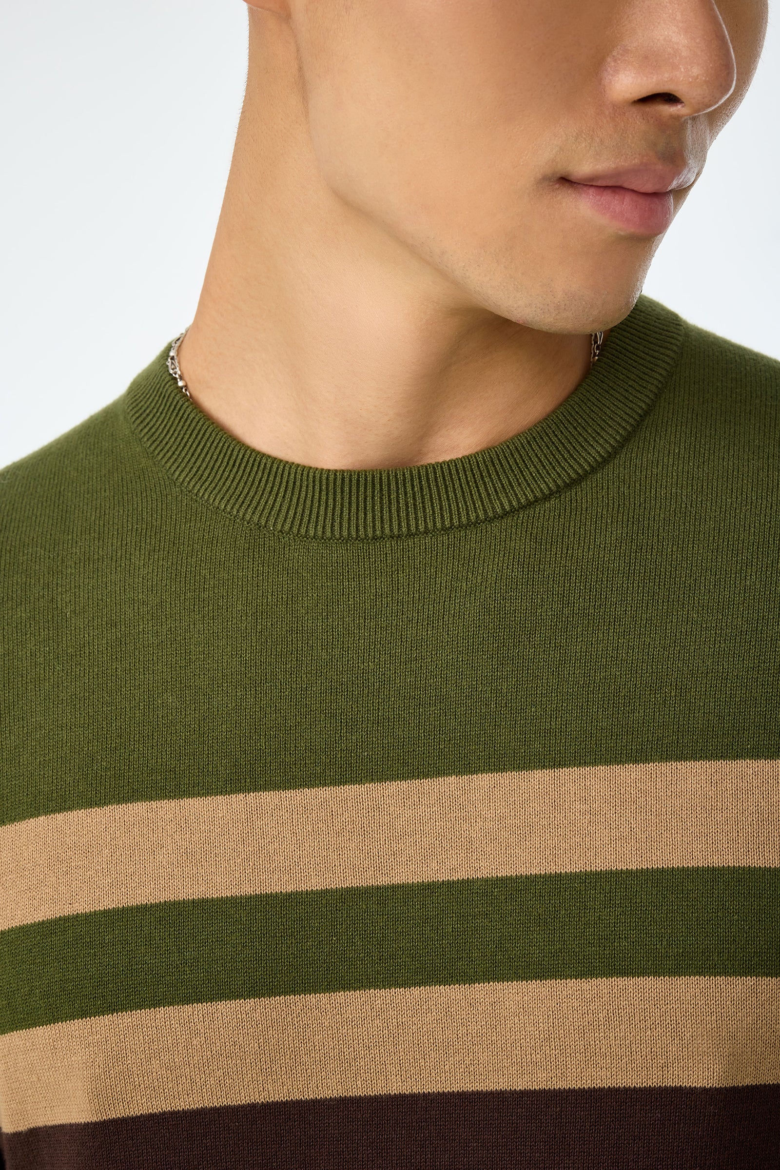 Close-up of a person wearing the Romero Crewneck Sweater in olive green with tan and dark brown stripes, showing the lower half of the face, neck, and upper chest.