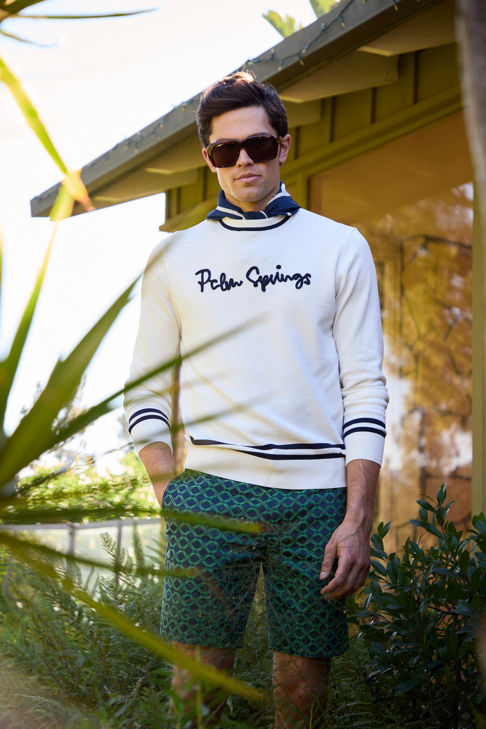 Man wearing a white sweater with 'Palm Springs' text and green shorts outdoors.