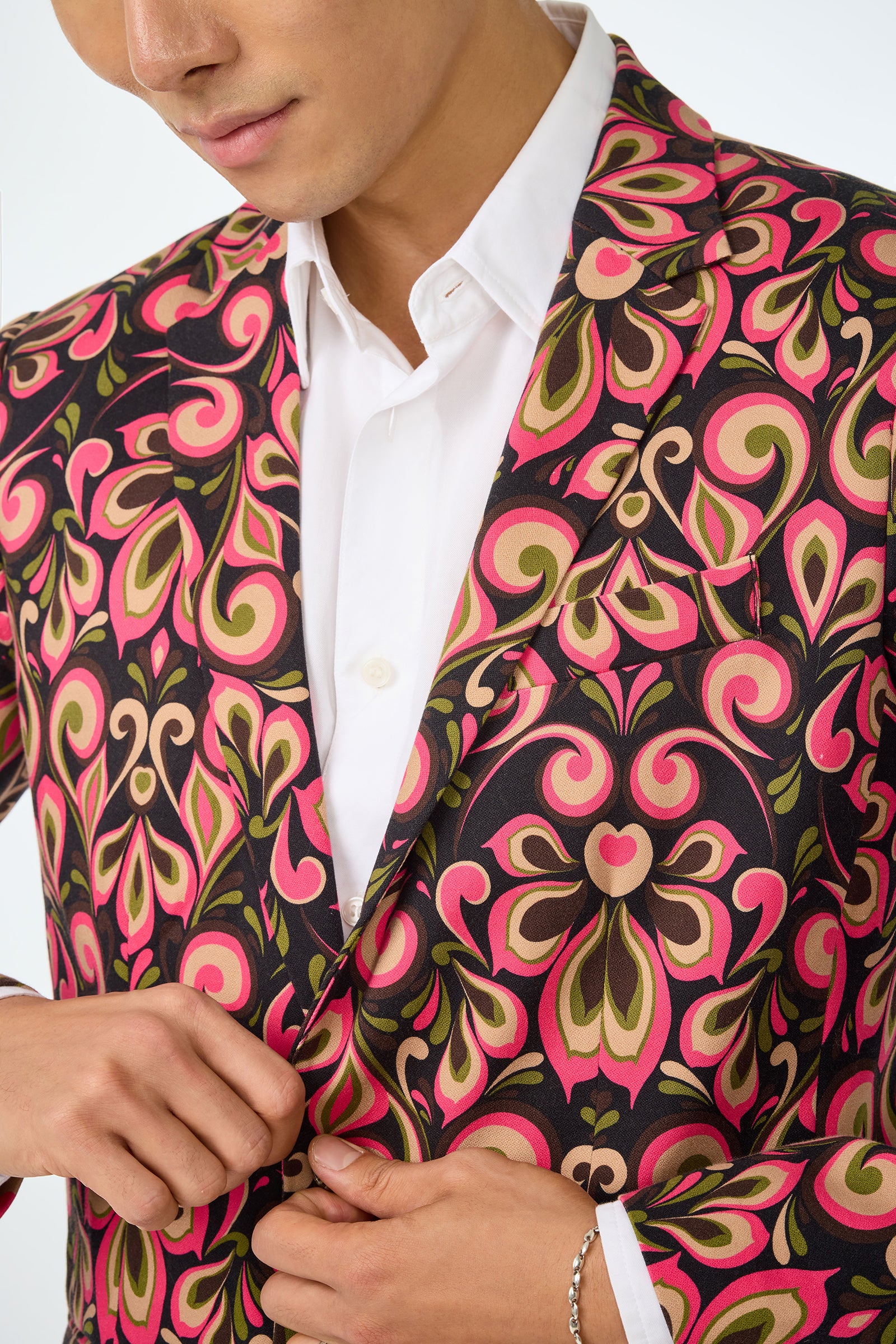 A person wearing a white dress shirt and the Thurston Blazer - Sanctuary, featuring bold pink, green, and black swirling patterns, is buttoning the jacket. Only their lower face and upper body are visible.