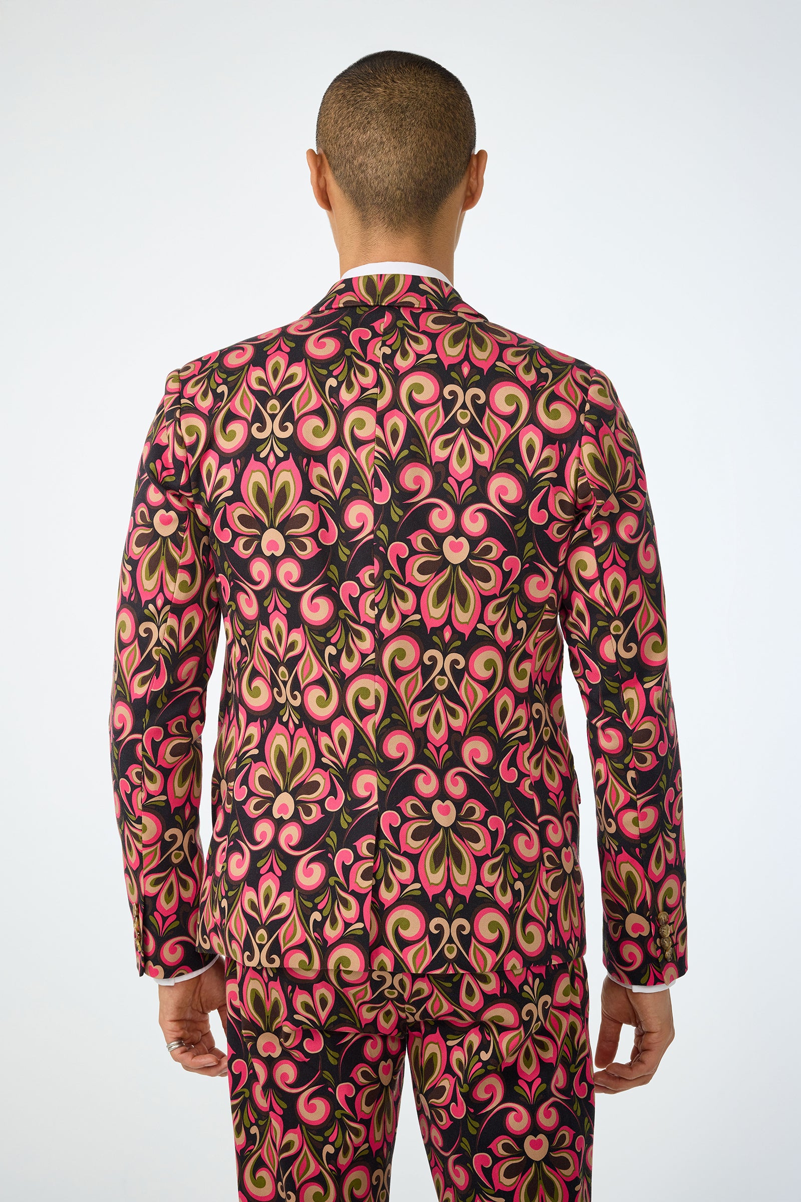 A person with short hair is seen from behind wearing the Thurston Blazer - Sanctuary, a fitted suit featuring bold pink, gold, and green abstract floral patterns on a black background.