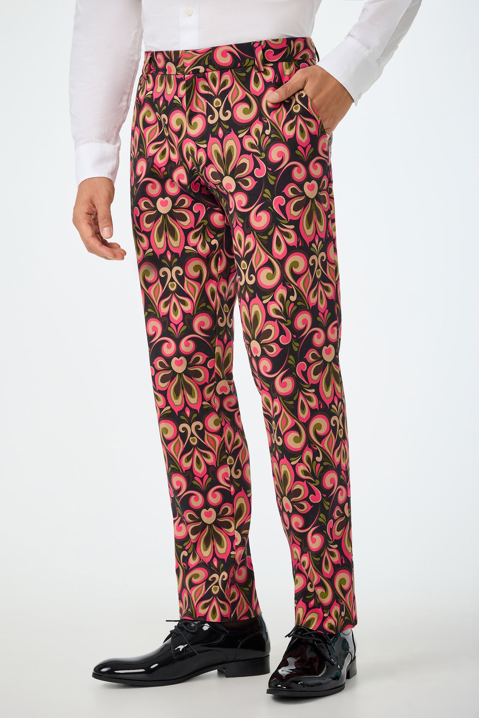 A person shown from the shoulders down wears a white dress shirt, shiny black dress shoes, and models the Clyde Slim Trouser - Sanctuary featuring a bold red, gold, and black floral pattern.
