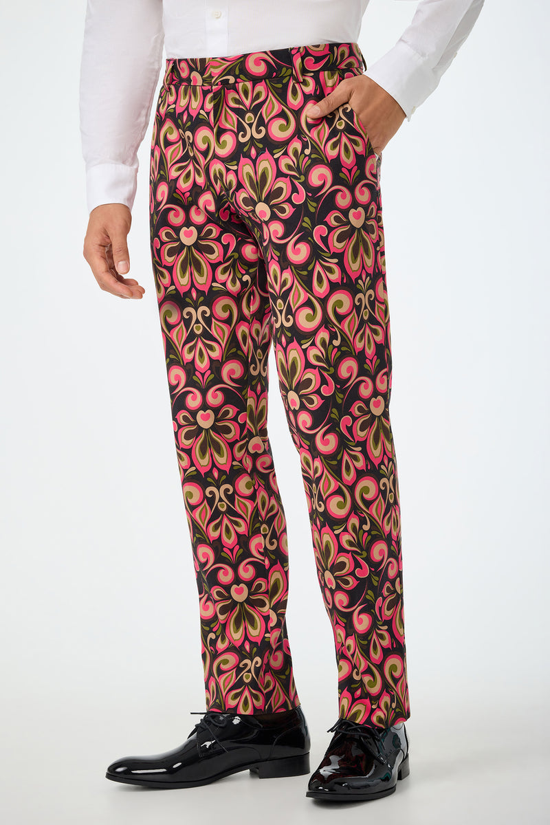 A person shown from the shoulders down wears a white dress shirt, shiny black dress shoes, and models the Clyde Slim Trouser - Sanctuary featuring a bold red, gold, and black floral pattern.