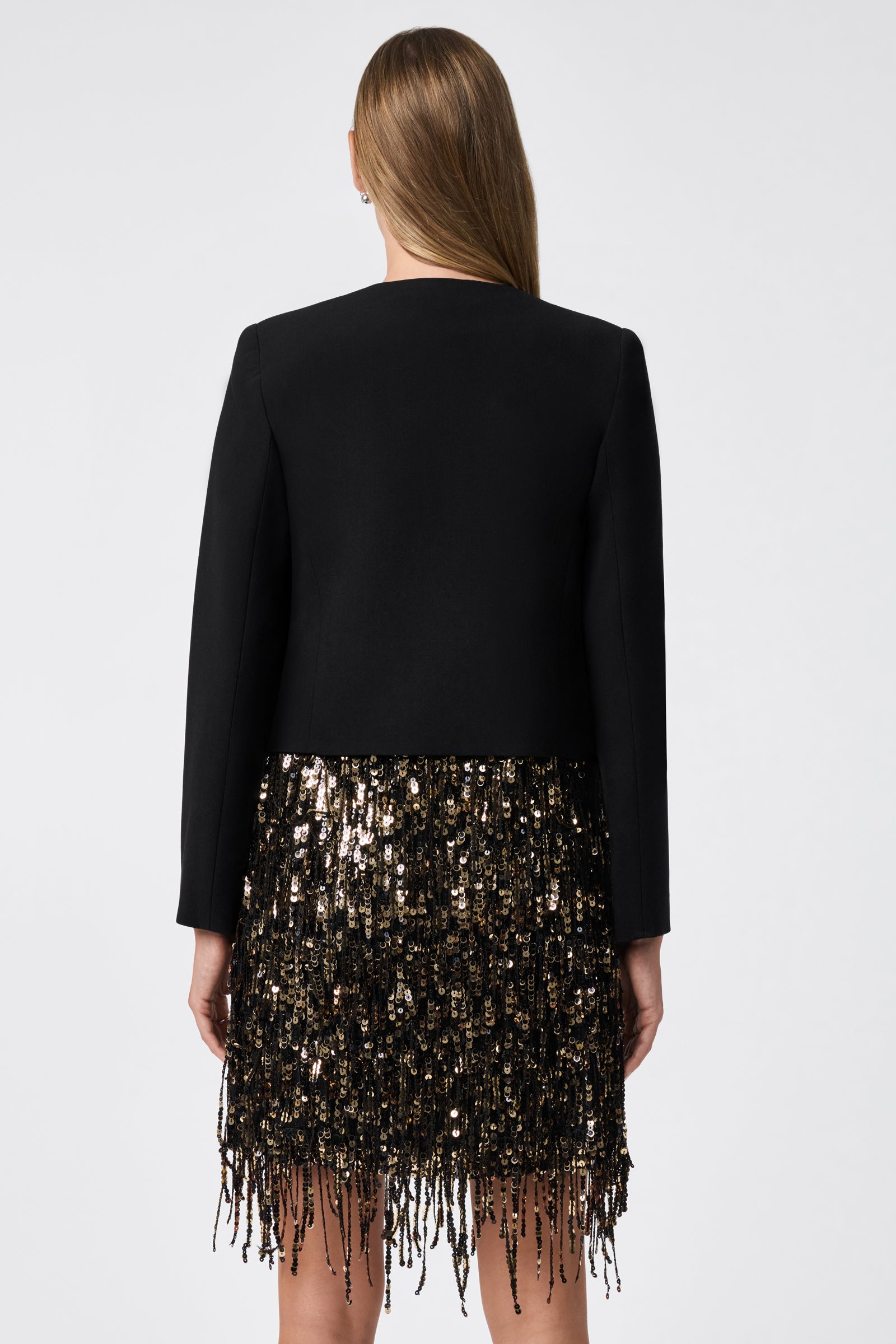 A woman stands facing away, wearing the Ren Cropped Long Sleeve Blazer Jacket in black against a plain light background.