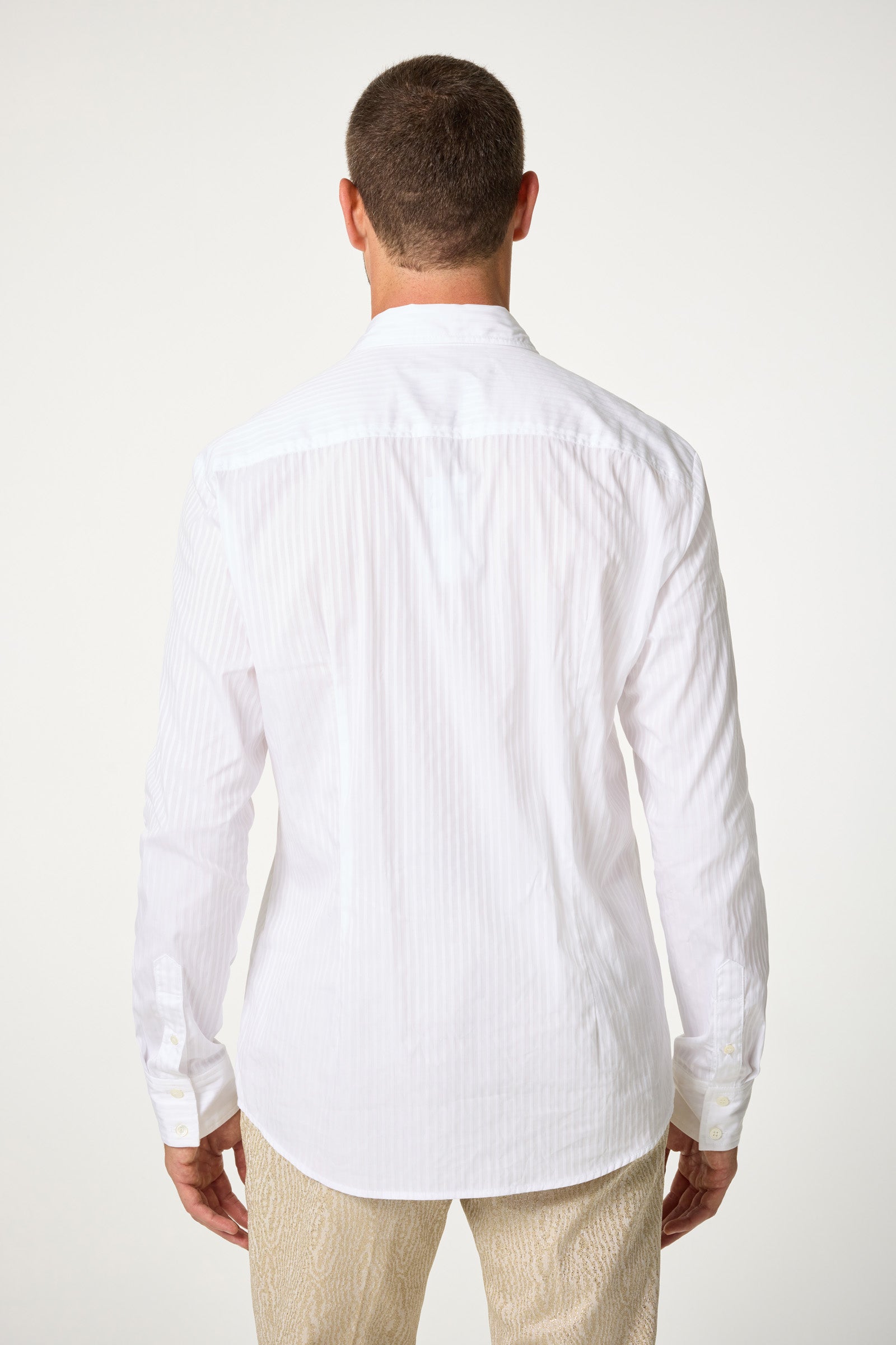A man is shown from behind wearing the Baleri Tux Shirt, a white long-sleeve dress shirt, along with light-patterned pants against a plain background.