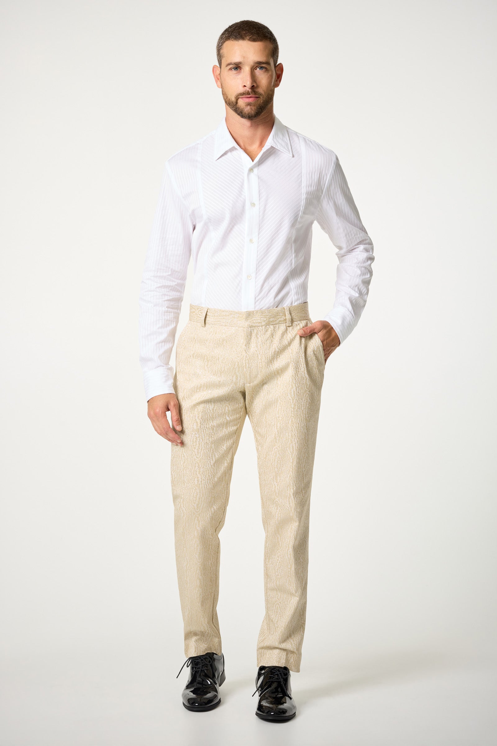 A man stands facing forward against a plain white background, wearing the Baleri Tux Shirt, beige textured trousers, and black dress shoes. One hand is in his pocket and he maintains a neutral expression.