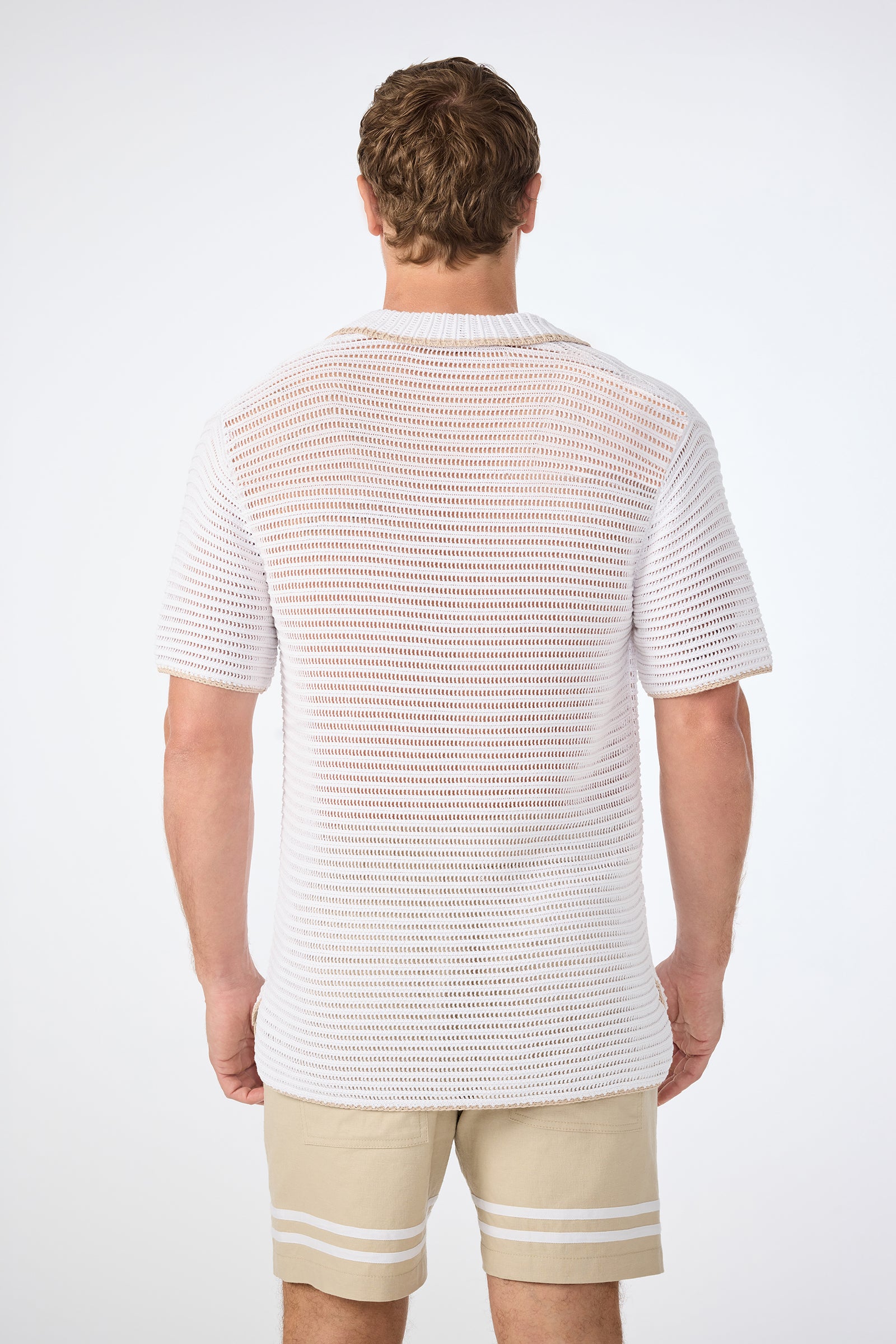 A man stands with his back to the camera, wearing the Triston Short-Sleeve Crochet Polo in white and beige shorts with white striped hems, set against a plain white background.