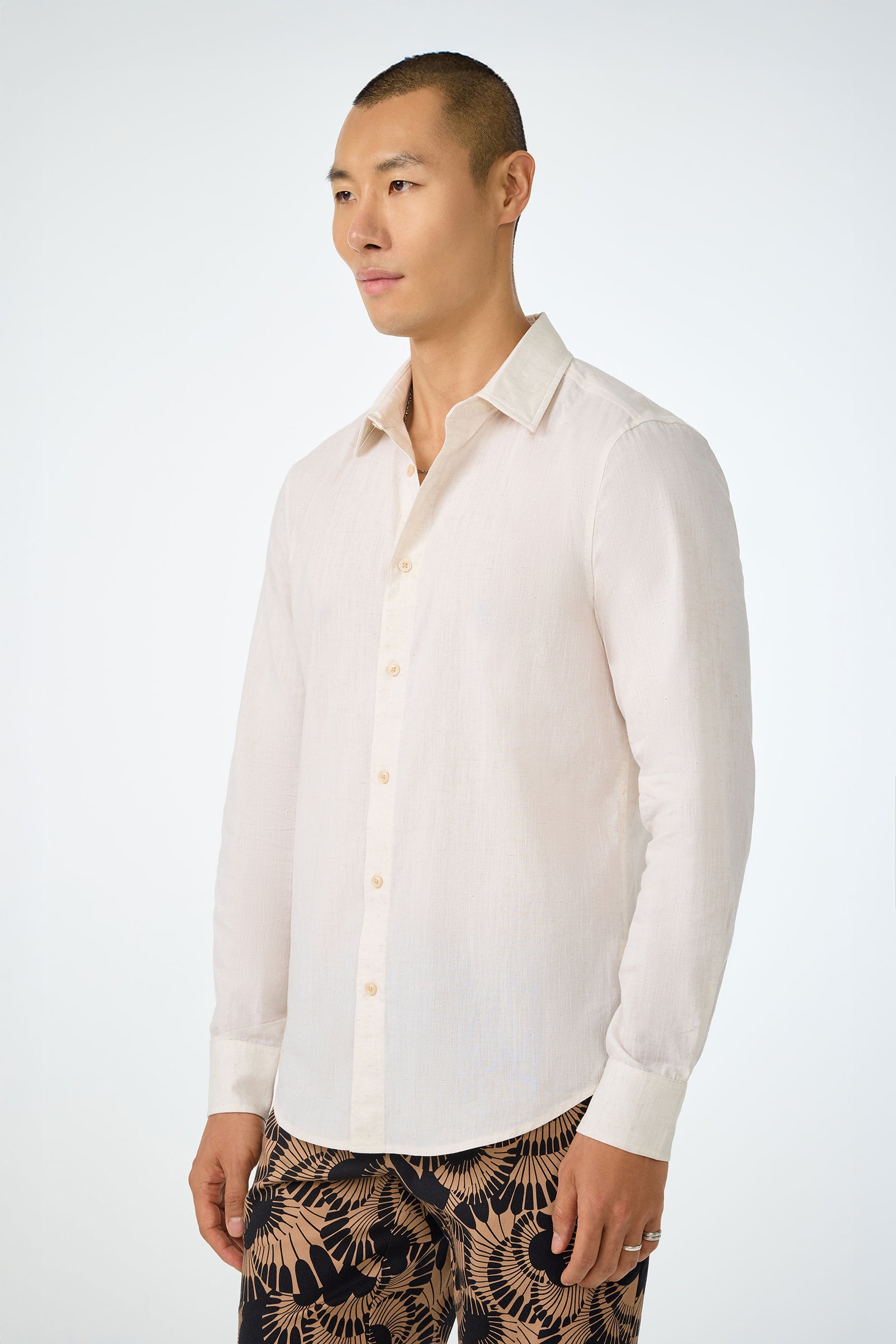 A man with short hair wears the Aaron Slim Fit Long-Sleeve Shirt in light beige and patterned black and beige pants, standing against a plain light background.
