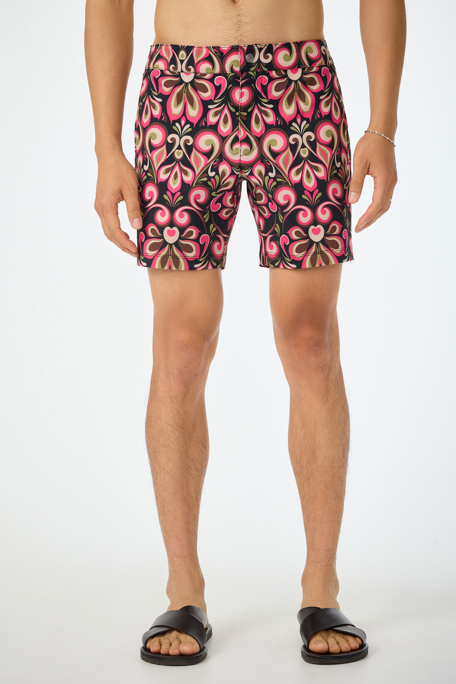 A person is wearing the Honolulu Board Short - Sanctuary, featuring a pink, black, cream, and green floral geometric design. Their upper body is not visible. The background is plain white.