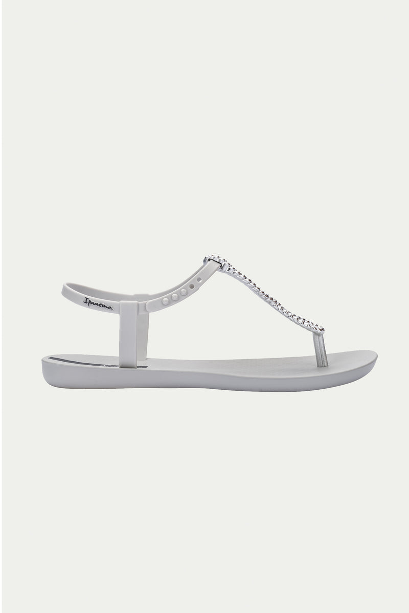 The Ipanema Class Twist Sandal in grey features a T-strap design with a thin ankle strap and a decorative chain detail down the center to the toe post. It has a simple, flat sole and offers a sleek, minimalist look.