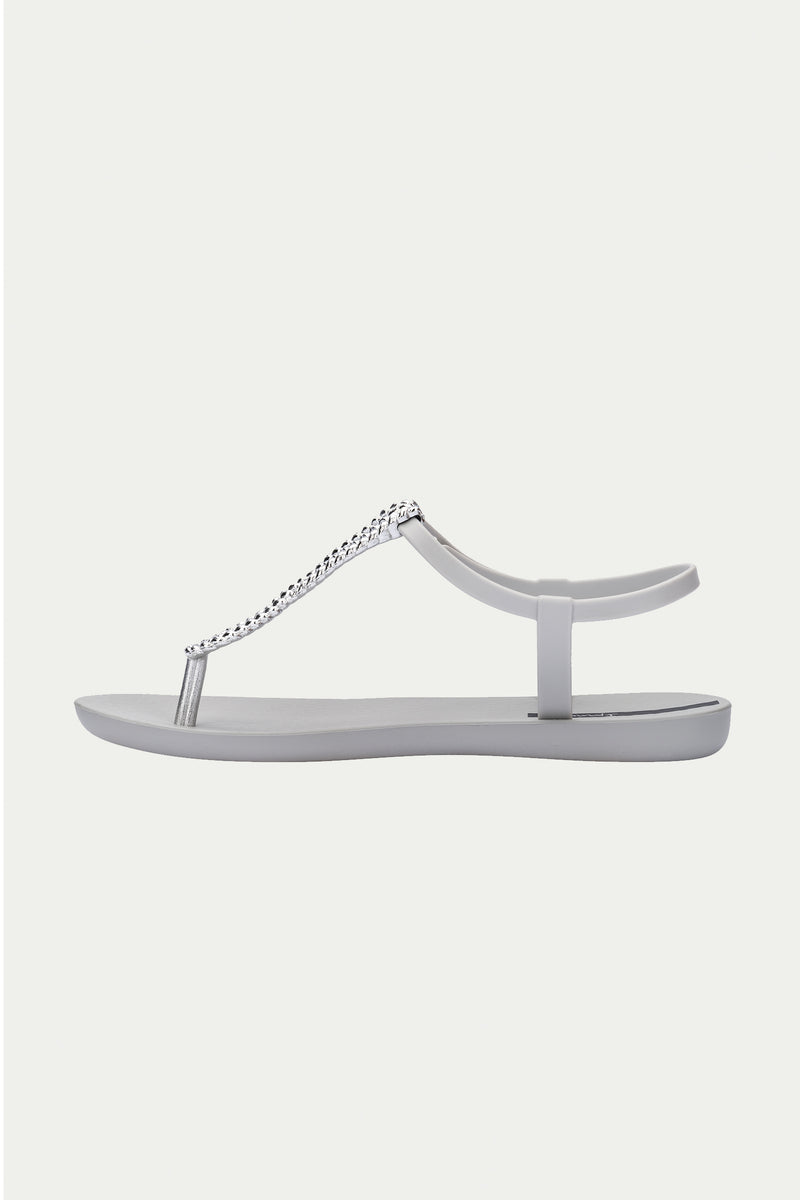 The Ipanema Class Twist Sandal in Grey is a minimalist flat sandal featuring a toe post, ankle strap, and a decorative silver chain detail across the top.