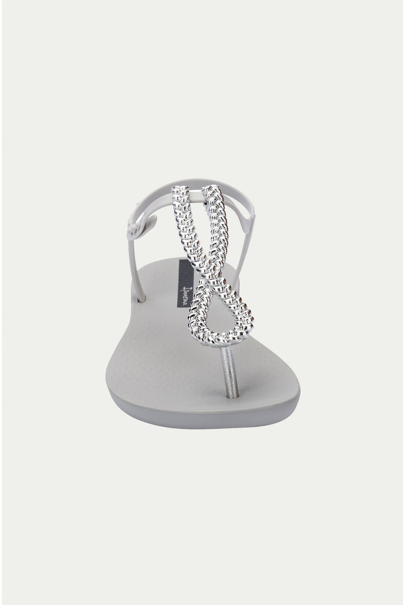 The Ipanema Class Twist Sandal in grey features a T-strap design with a silver, rhinestone-encrusted decorative loop on the upper strap, shown from the front against a plain white background.