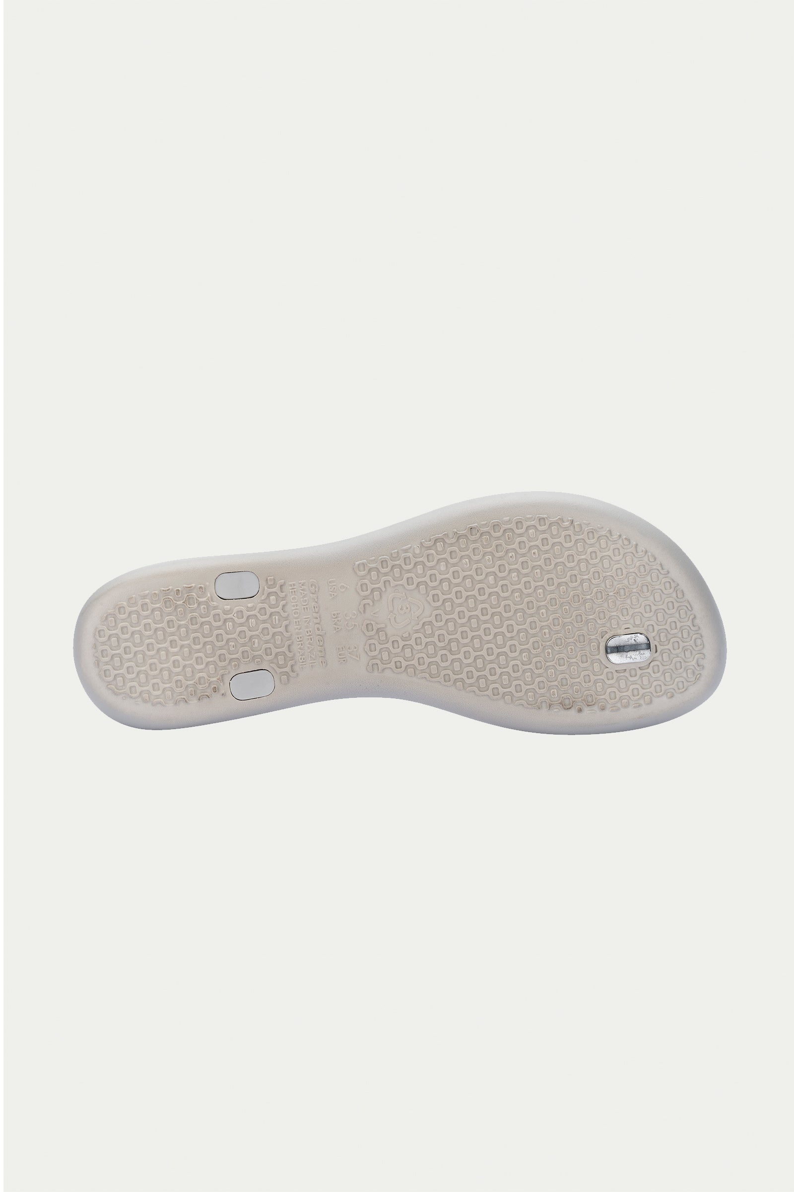The Ipanema Class Twist Sandal in grey is shown from the bottom, highlighting its textured sole for grip and two small metallic accents embedded in the heel and midfoot areas.