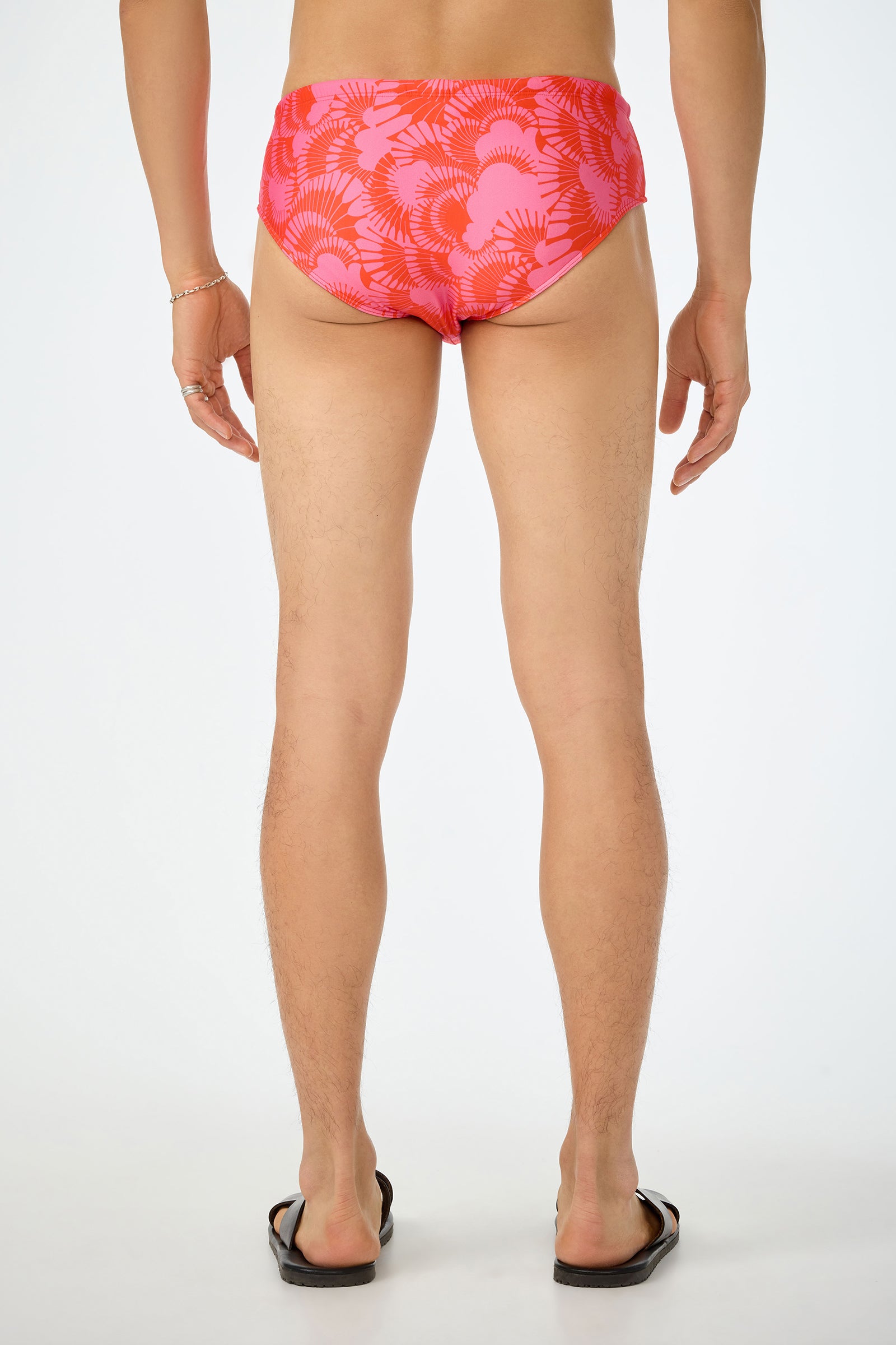 A person with their back to the camera wears the San Gregorio Swim Brief - Juniper and black flip-flops, standing against a plain white background.