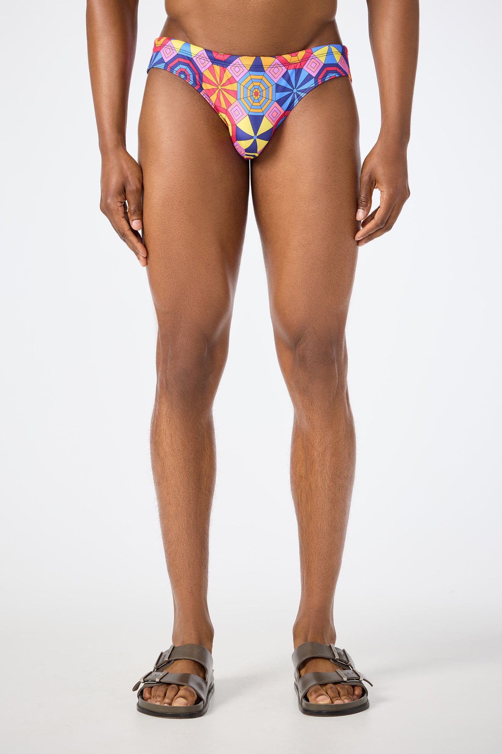 A person faces forward wearing the Bondi Swim Brief - Parasol in multi, paired with brown sandals. The image is cropped from the shoulders down against a plain white background.