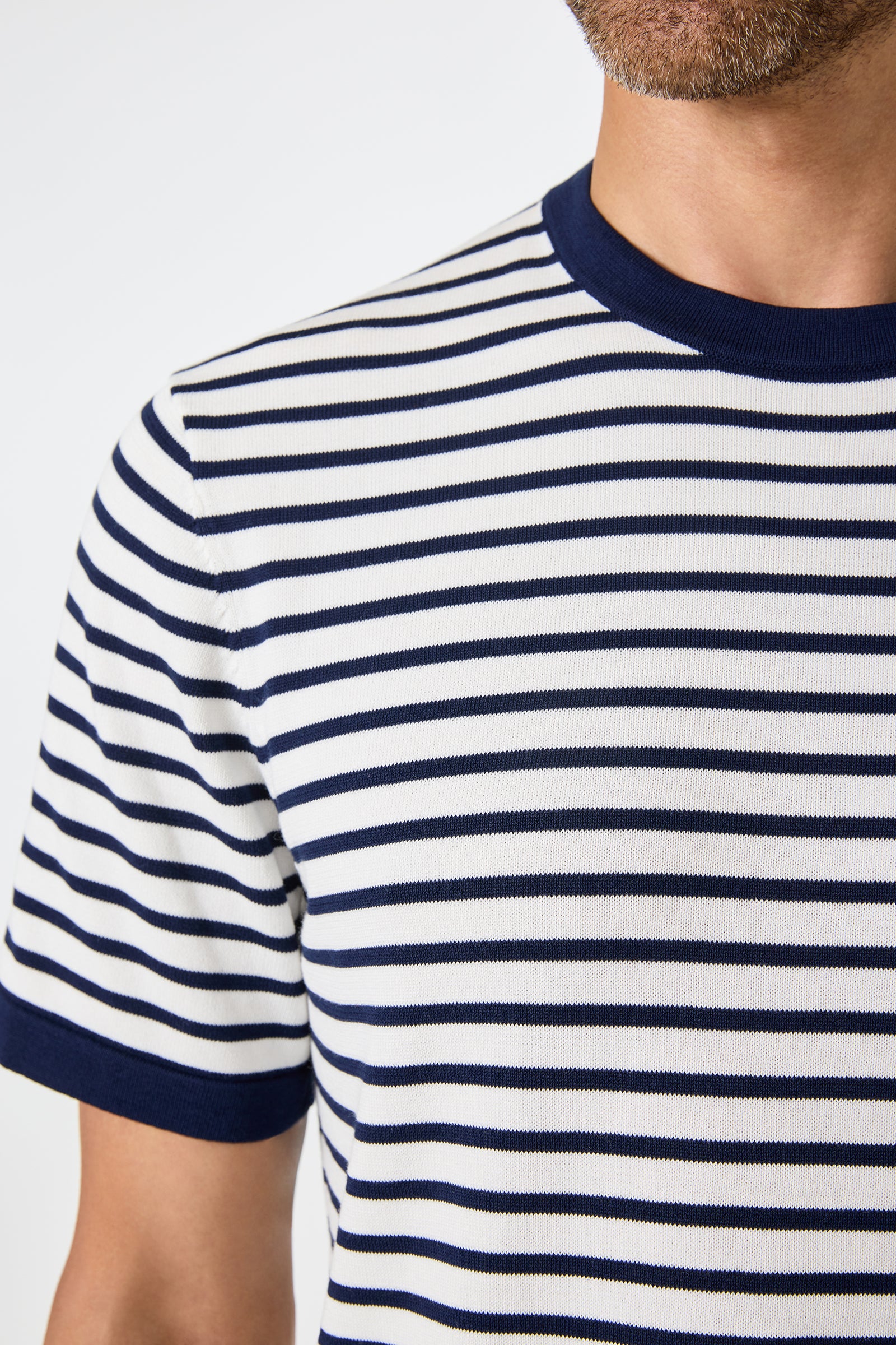 Close-up of a person wearing the Giovanni Stripe Short-Sleeve Pullover, featuring white fabric with horizontal navy stripes and navy trim on the collar and sleeve cuffs. Only the lower face and upper torso are visible.