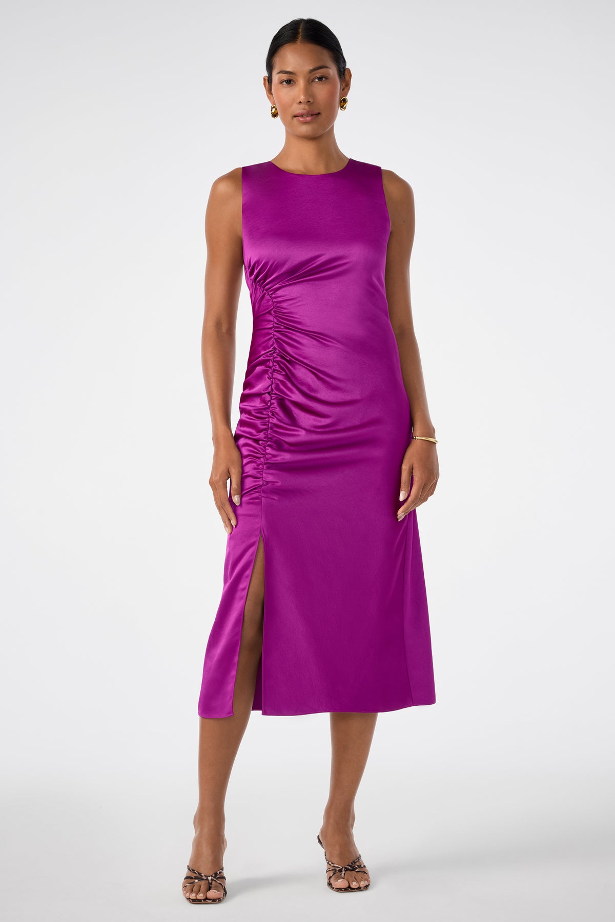 A woman wears the Chestnut Dress, a sleeveless magenta midi with side ruching and a front slit, styled with heeled sandals and minimal jewelry against a plain white background.