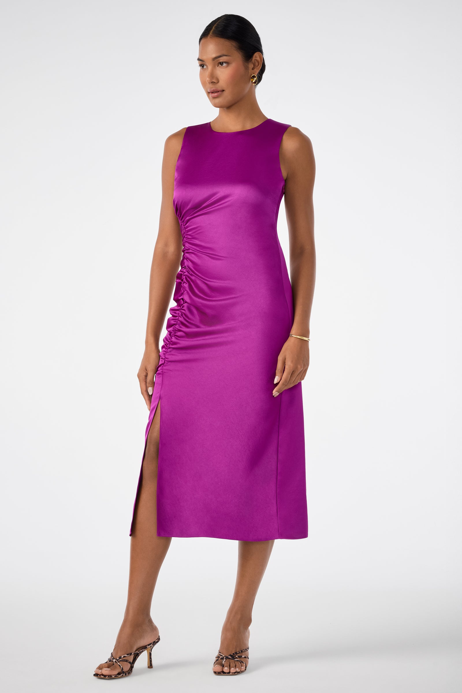 A woman in the Chestnut Dress, a sleeveless bright magenta midi with side ruching and a thigh-high slit, pairs it with animal-print heeled sandals and minimal jewelry, standing against a white background.