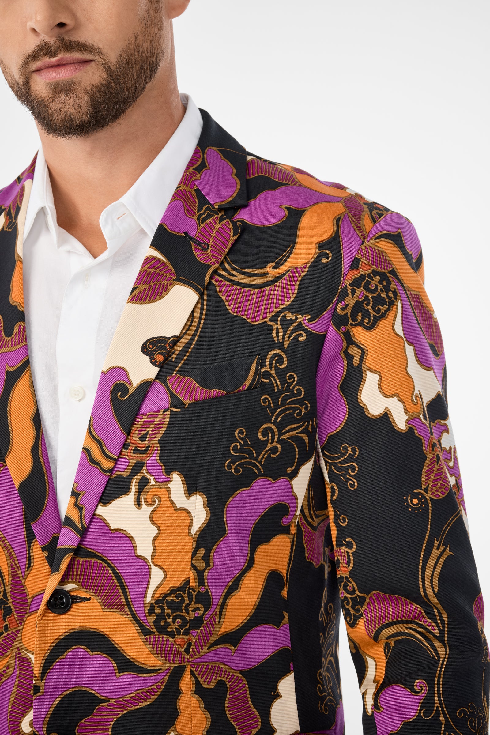 A man with a beard wears the Thurston Blazer, featuring an abstract floral pattern in purple, orange, black, and cream over a white shirt. The image shows him from chest to head with his face partially visible.