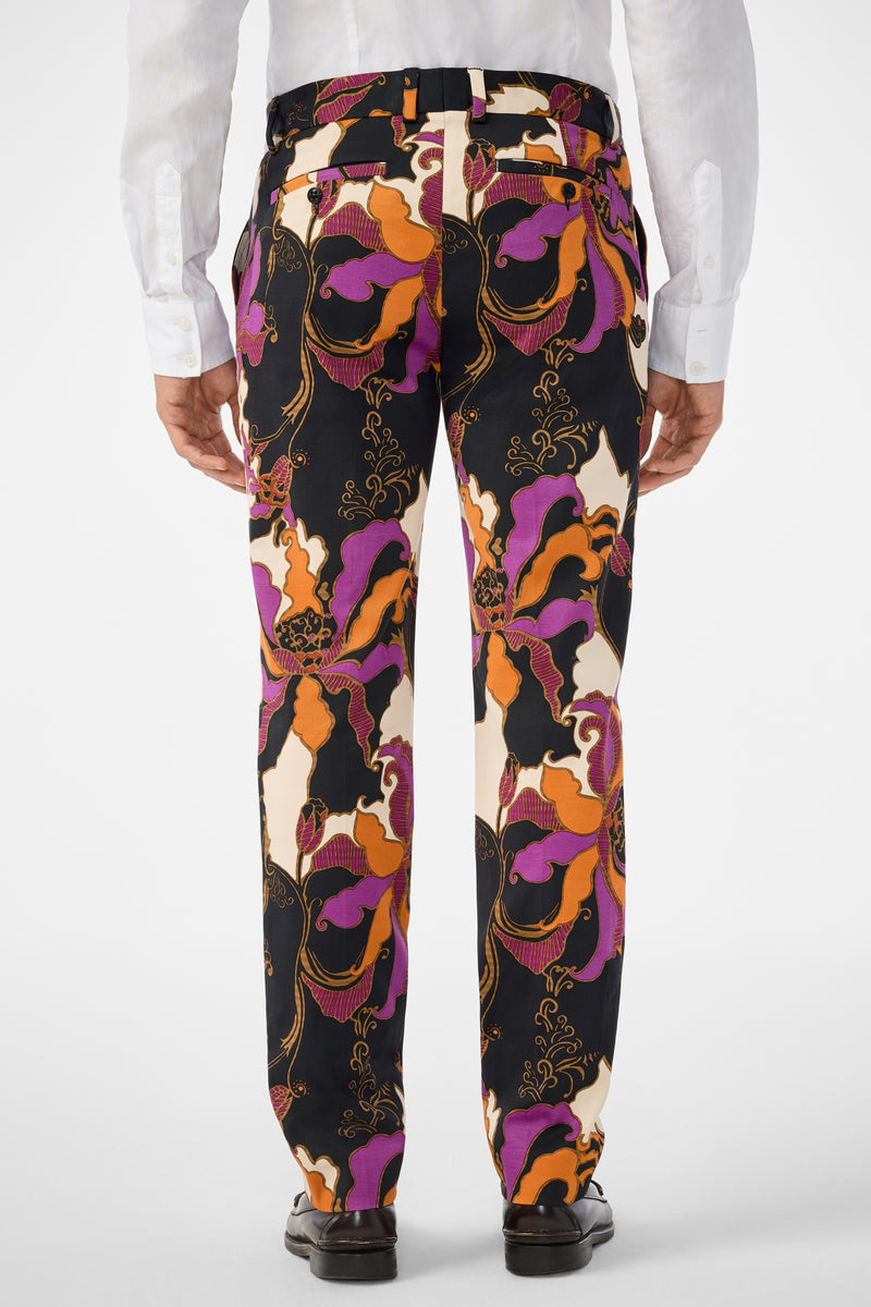 A person is shown from the back against a plain light background, wearing black dress shoes, a white dress shirt, and Clyde Slim Trouser featuring colorful patterns in orange, purple, black, and cream.