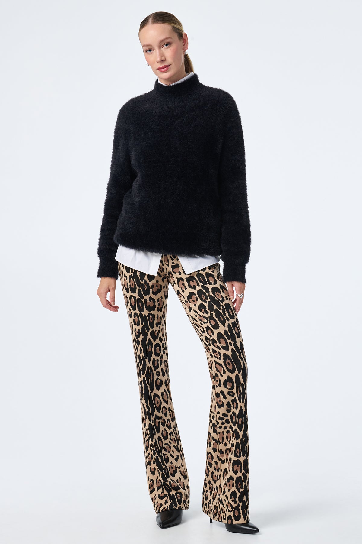 A woman poses against a plain background in a black fuzzy sweater over a white shirt, styled with Jacoba Slim-Fit Bootcut Pants in beige leopard print and black pointed shoes.