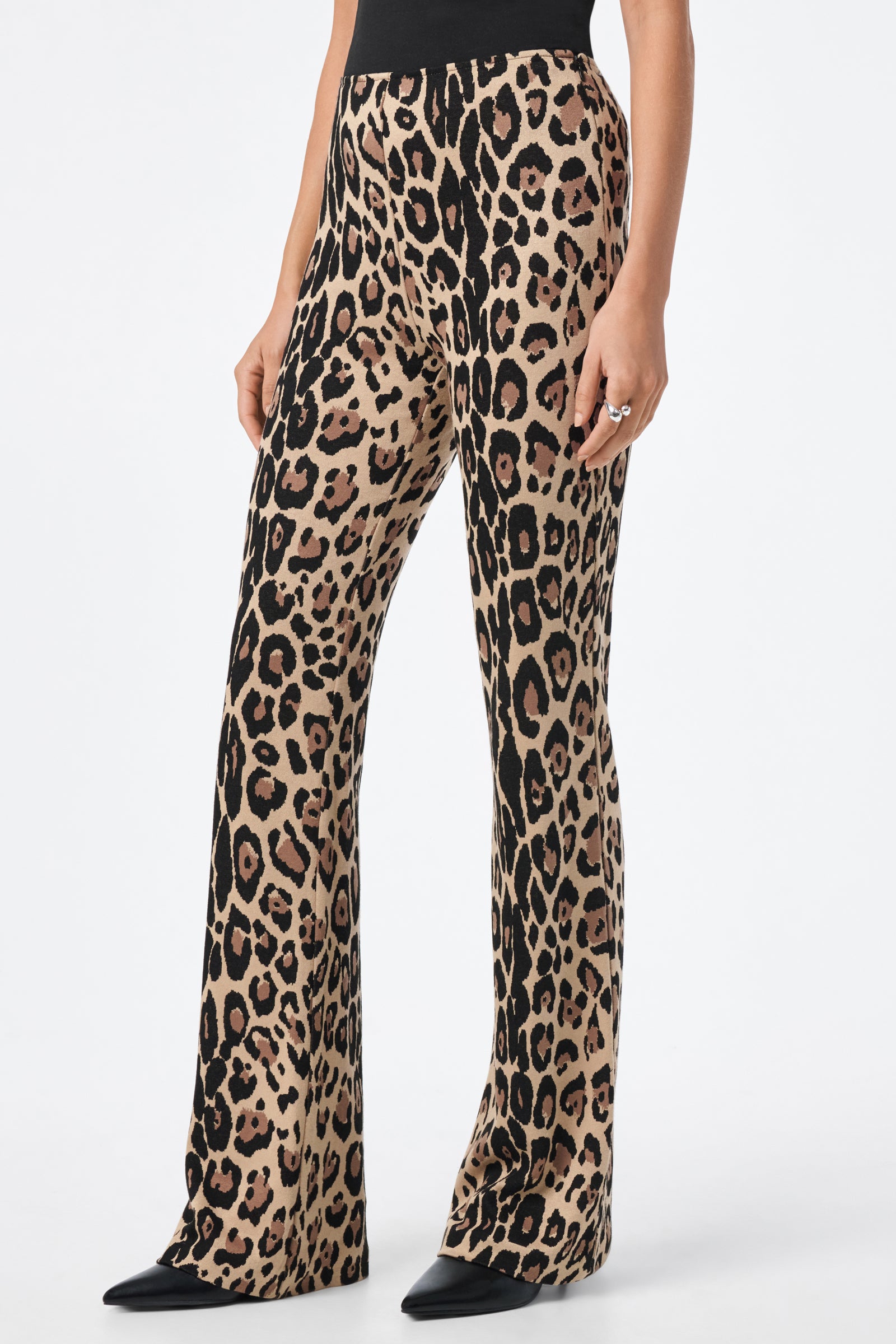 A person wearing the Jacoba Pant—high-waisted, flared pants with a bold leopard print—paired with a black top and pointed black shoes.