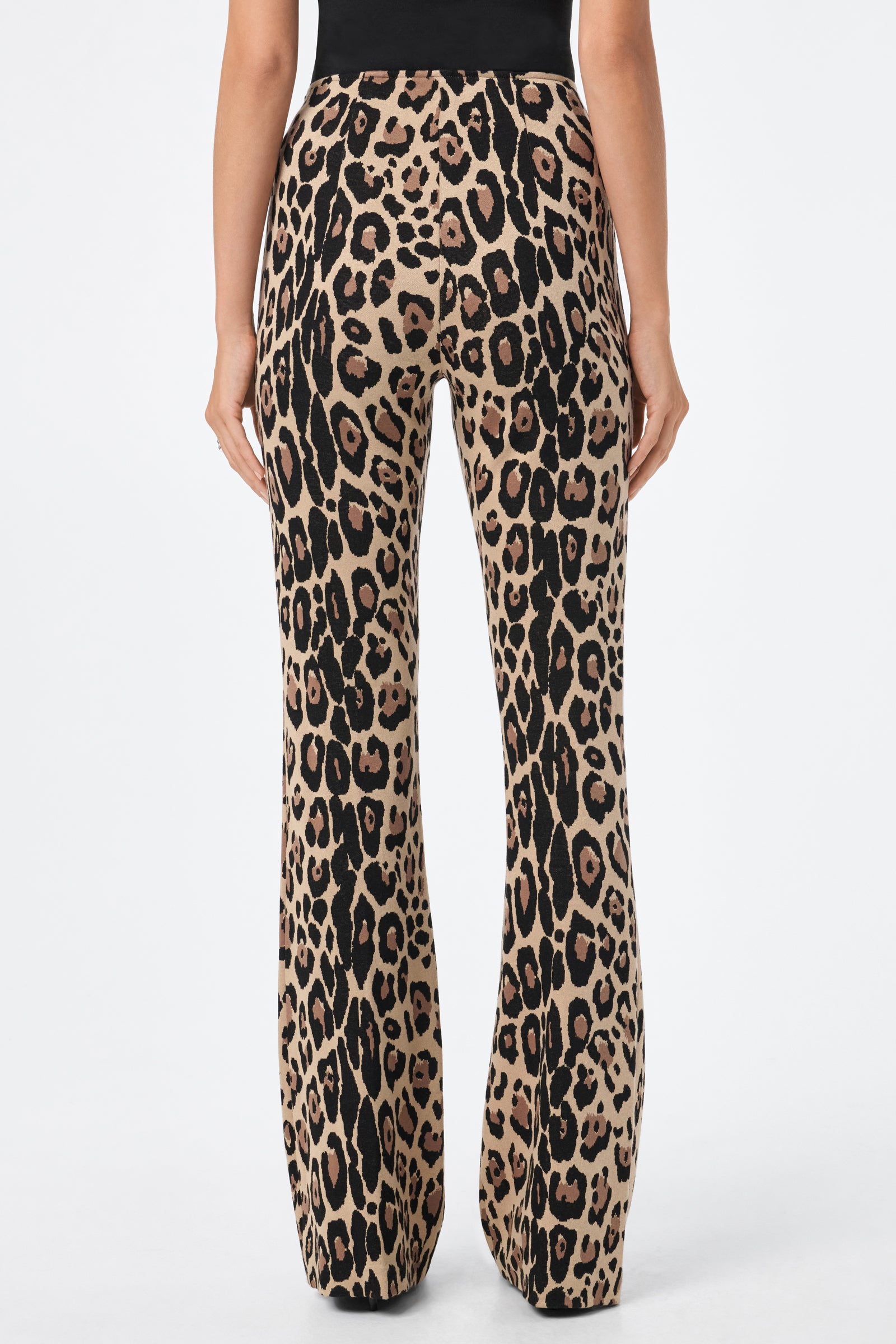 A person shown from the back wears the Jacoba Pant, featuring a high-waisted, flared silhouette with a bold leopard print pattern, set against a plain white background.