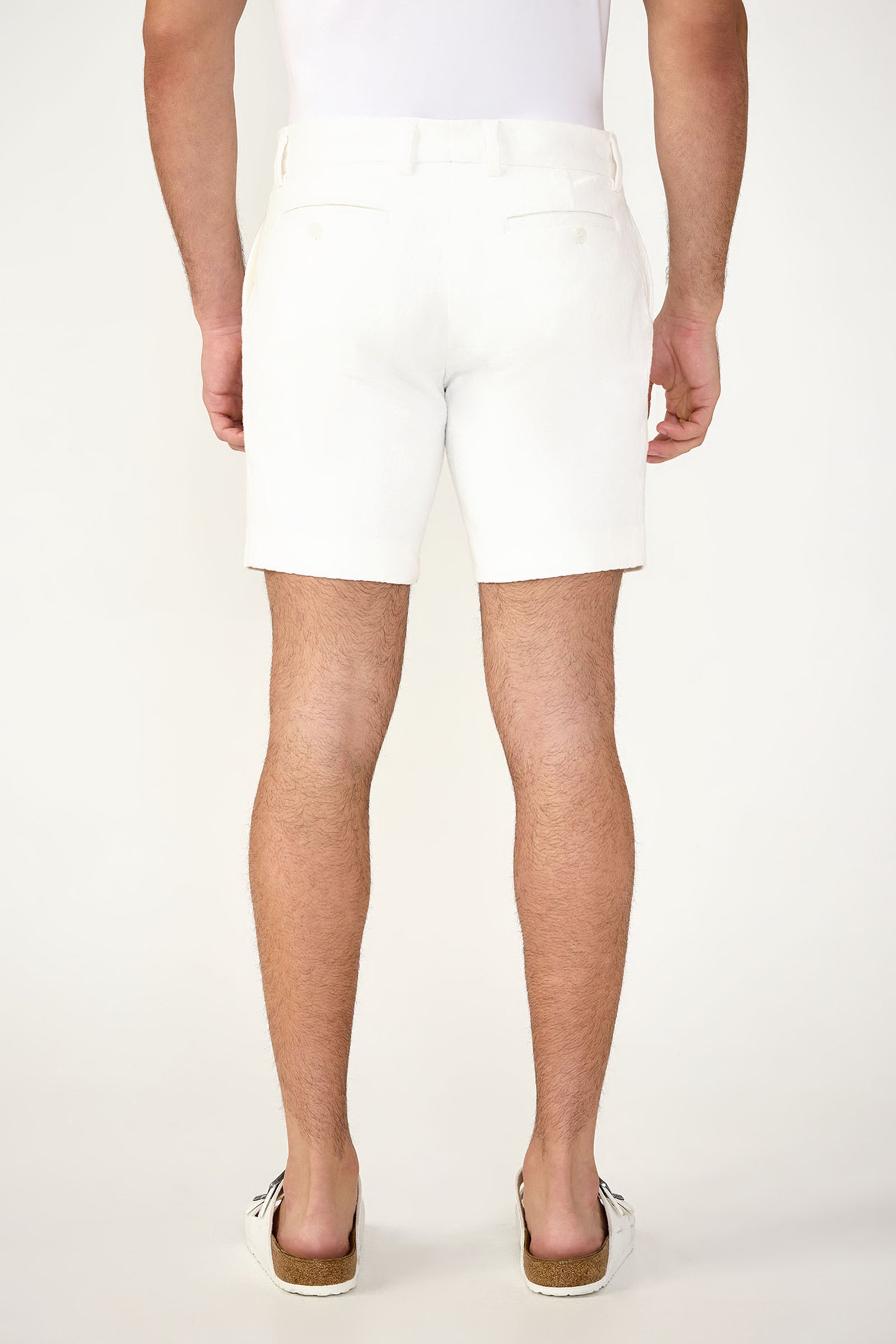 A person stands facing away from the camera in the Lawrence Short - Stretch Herringbone and a matching white top with white slip-on shoes featuring brown soles, set against a plain white background.