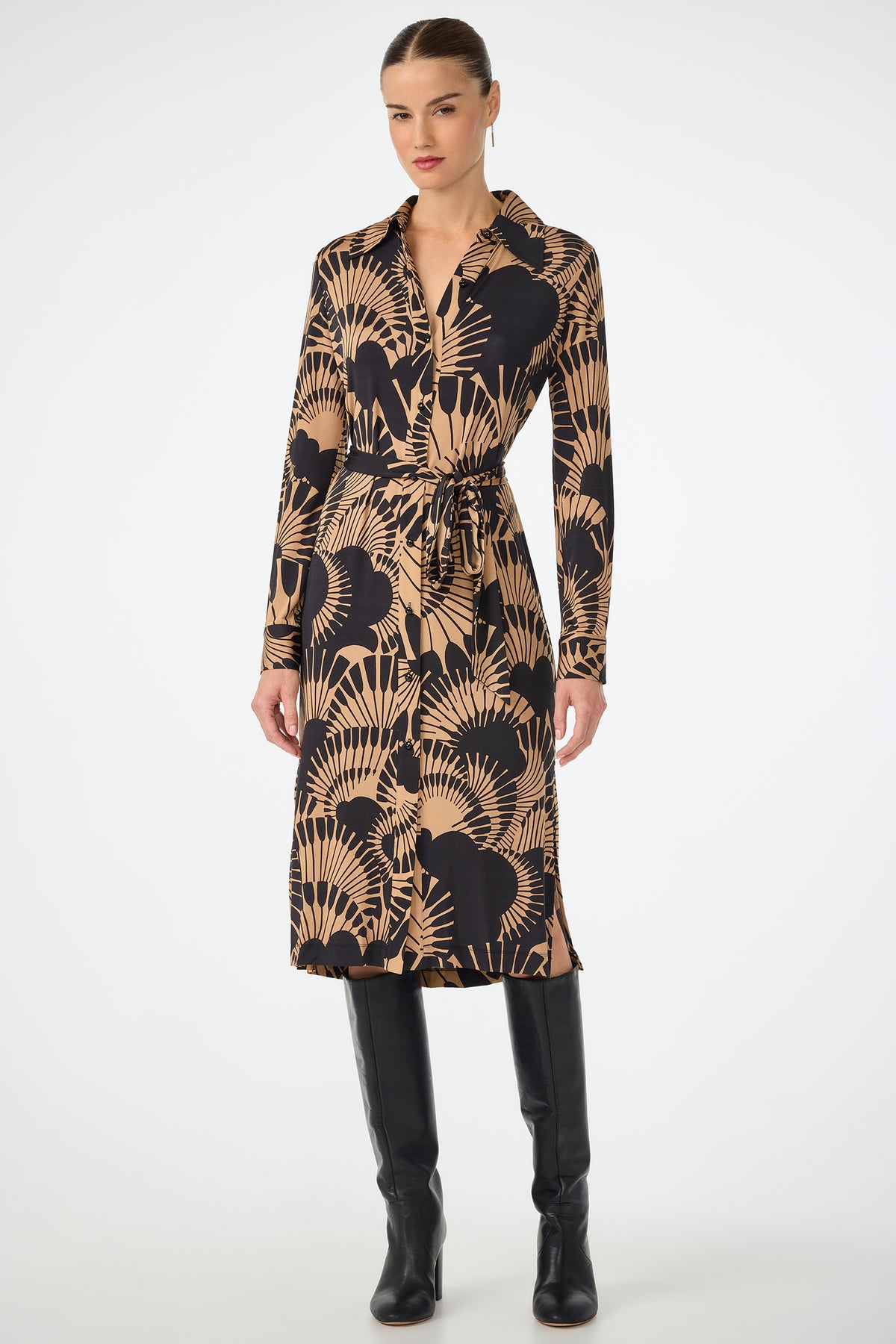 A woman wearing the Radio City Wrap Dress in Juniper Jersey—a long-sleeve, collared, button-down dress with a tie belt—stands against a plain white background. She pairs it with knee-high black boots.