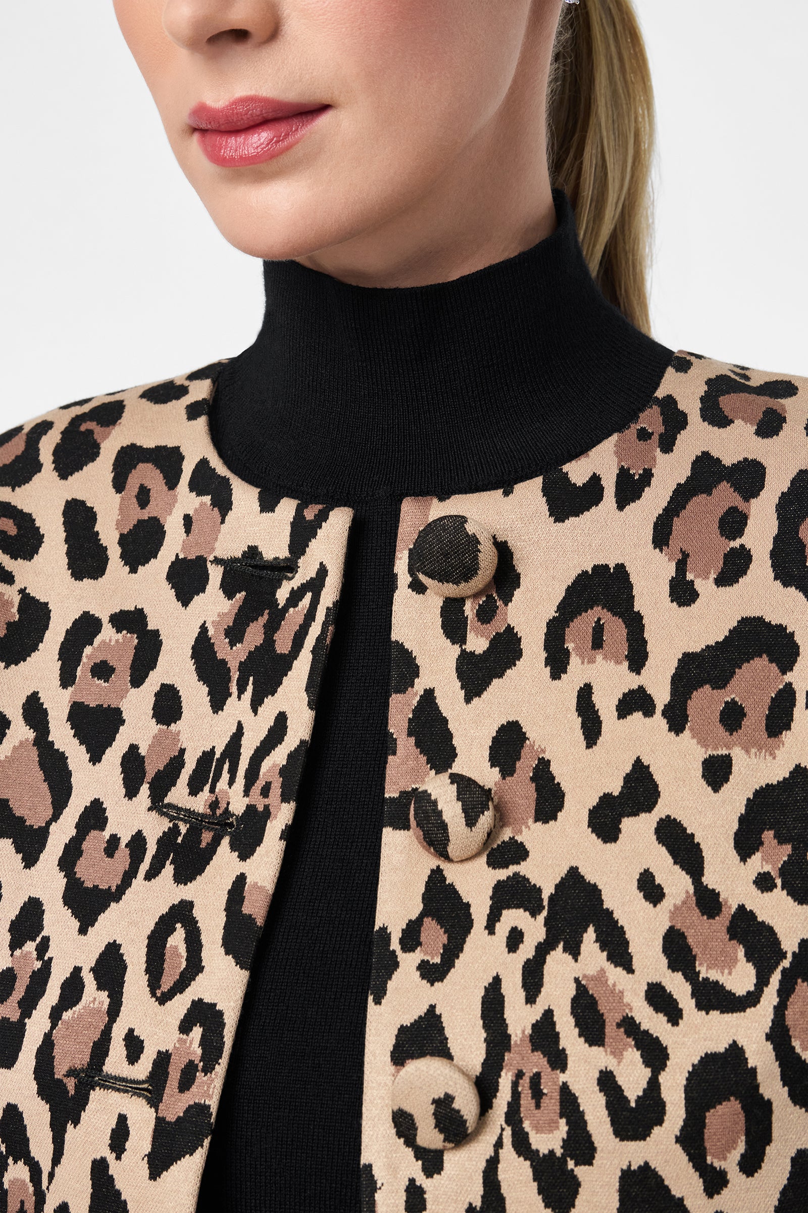 A woman wears the Critique Jacket, a beige and black leopard print coat with large buttons, layered over a black turtleneck. Only her lower face and torso are shown.