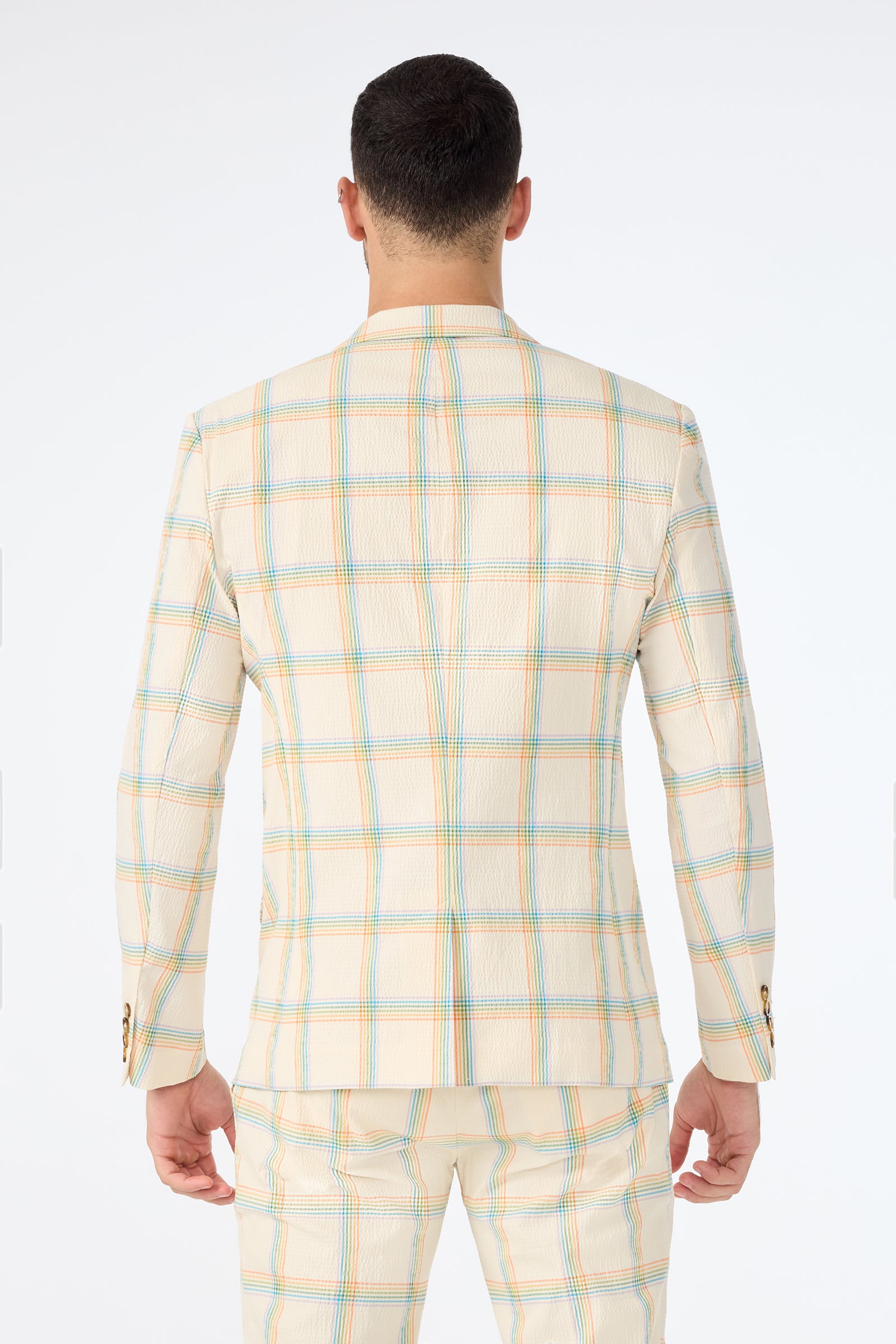 A man is seen from behind wearing the Louie Blazer - Pride Plaid, a cream-colored suit featuring a blue, yellow, and red plaid pattern, standing against a plain white background.