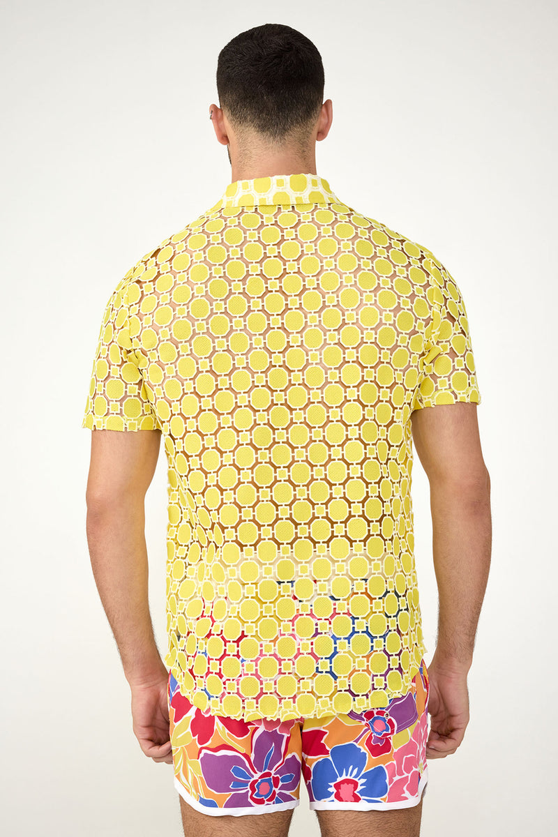 A man is seen from behind wearing the Long Beach Short-Sleeve Shirt, which is yellow with a geometric circular pattern, paired with colorful floral shorts featuring red, blue, and yellow flowers on a white background.