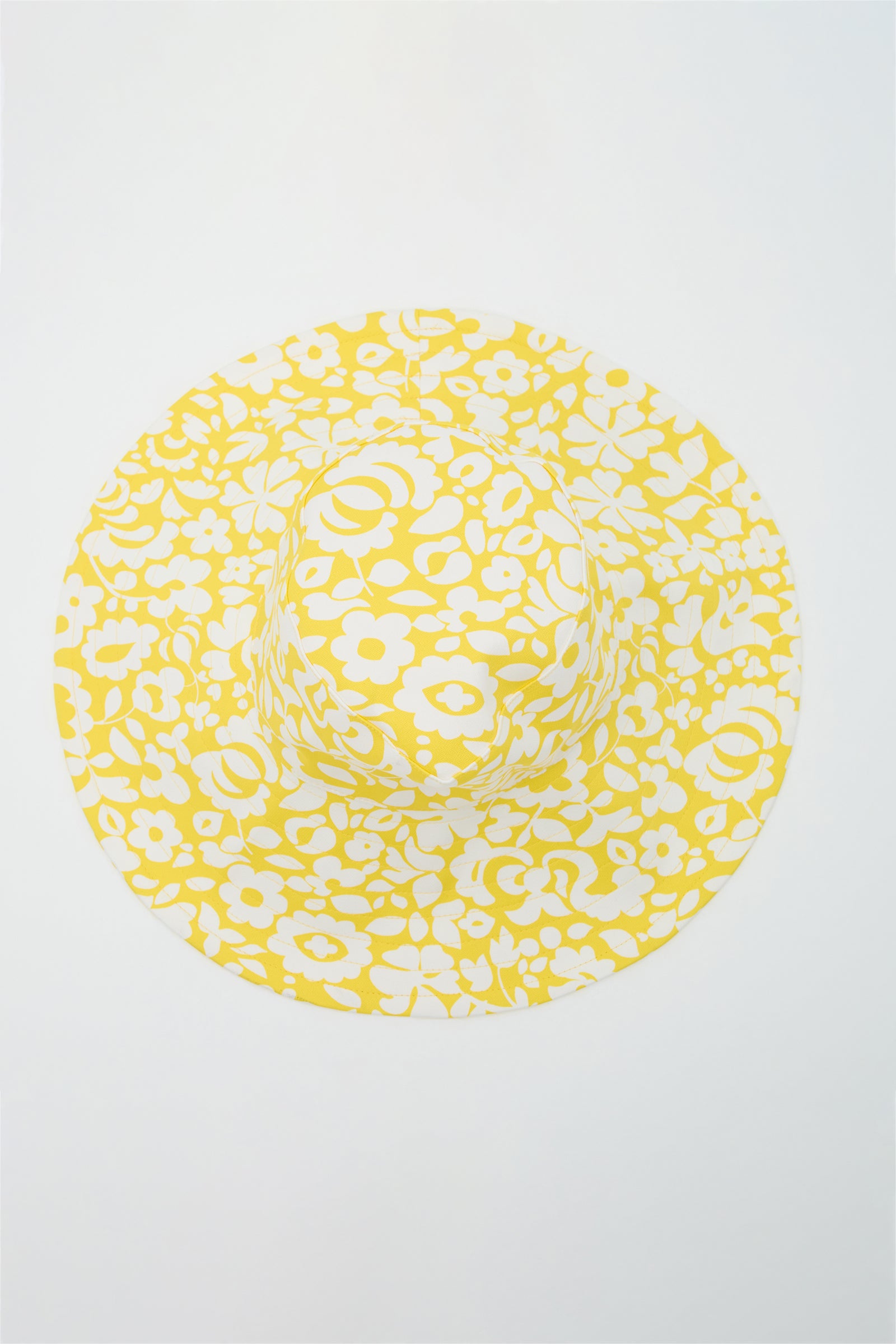 The Shade Packable Sun Hat - Poolside Gossip features a yellow and white floral pattern and a wide brim, shown from above against a plain white background.