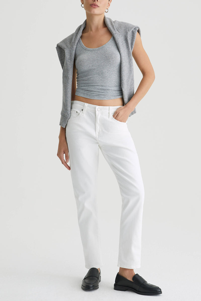 A person wearing a gray tank top, a gray sweater draped over their shoulders, AG Mid-Rise Slouchy Ex Boyfriend Jean - White, and black loafers stands against a plain white background.