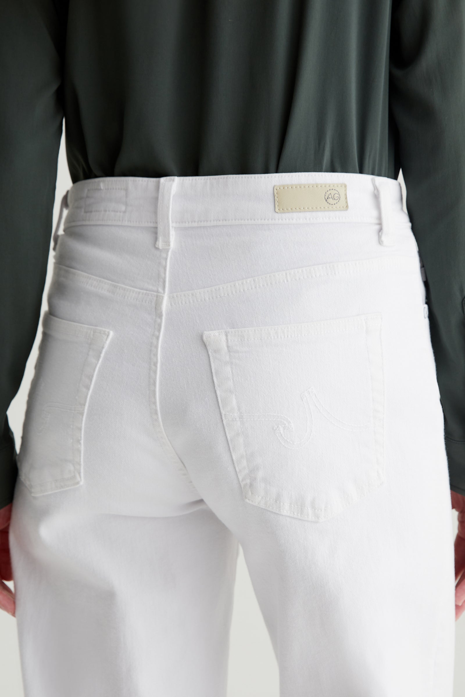 A person is shown from the back wearing white AG Saige Mid-Rise Wide-Leg Crop Jeans, with focus on the jeans rear pockets and waistband.