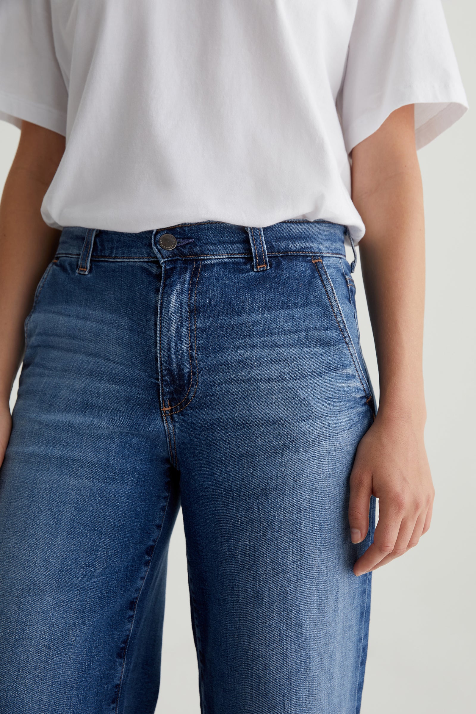 A person wearing a white t-shirt and AG Stella Low-Rise Palazzo Jeans in Indigo, shown from shoulders to thighs, with one hand by their side.