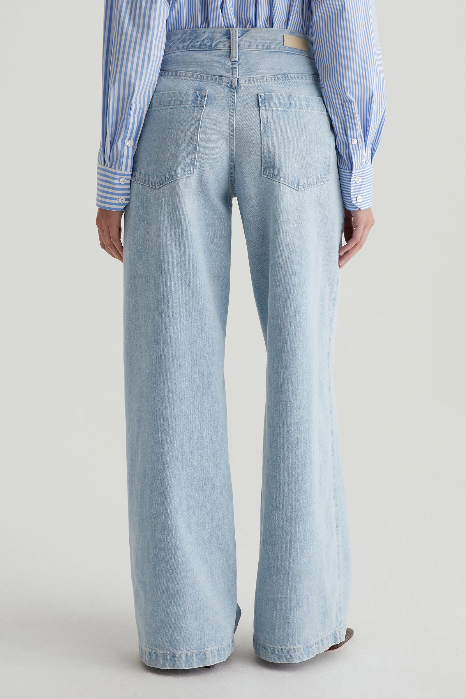 Someone is seen from the back wearing a blue and white striped shirt paired with AG Stella Low-Rise Palazzo Jeans in light blue, set against a plain light background.