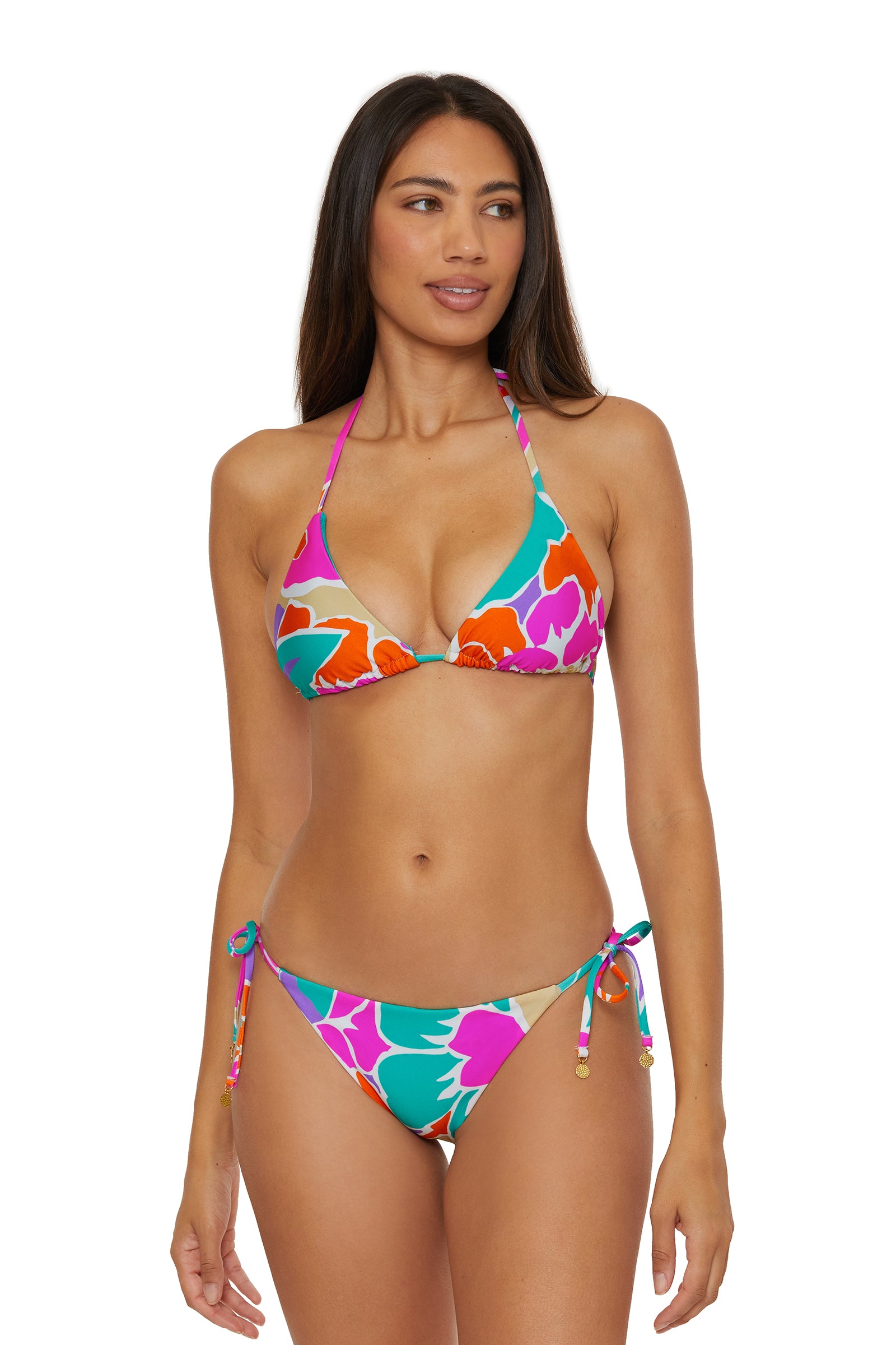 A woman models the Tie Side Hipster Swim Bottom - Amalfi, featuring a colorful floral print and side-tie details, paired with a halter bikini top. She stands against a white background, looking slightly right with a relaxed expression.