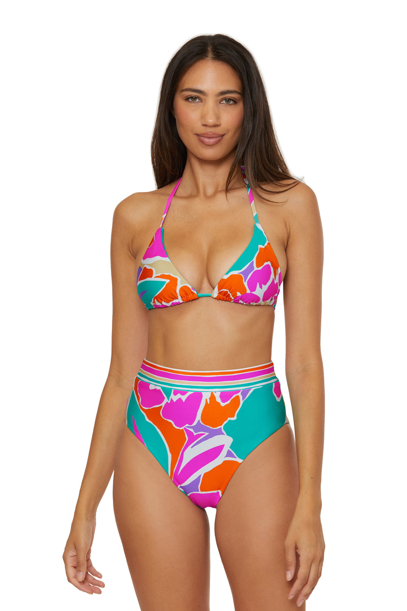 Woman wearing the High-Waist Swim Bottom - Amalfi, a colorful floral bikini with a halter-neck top and high-waisted bottoms in pink, orange, red, and green patterns, standing against a plain white background.