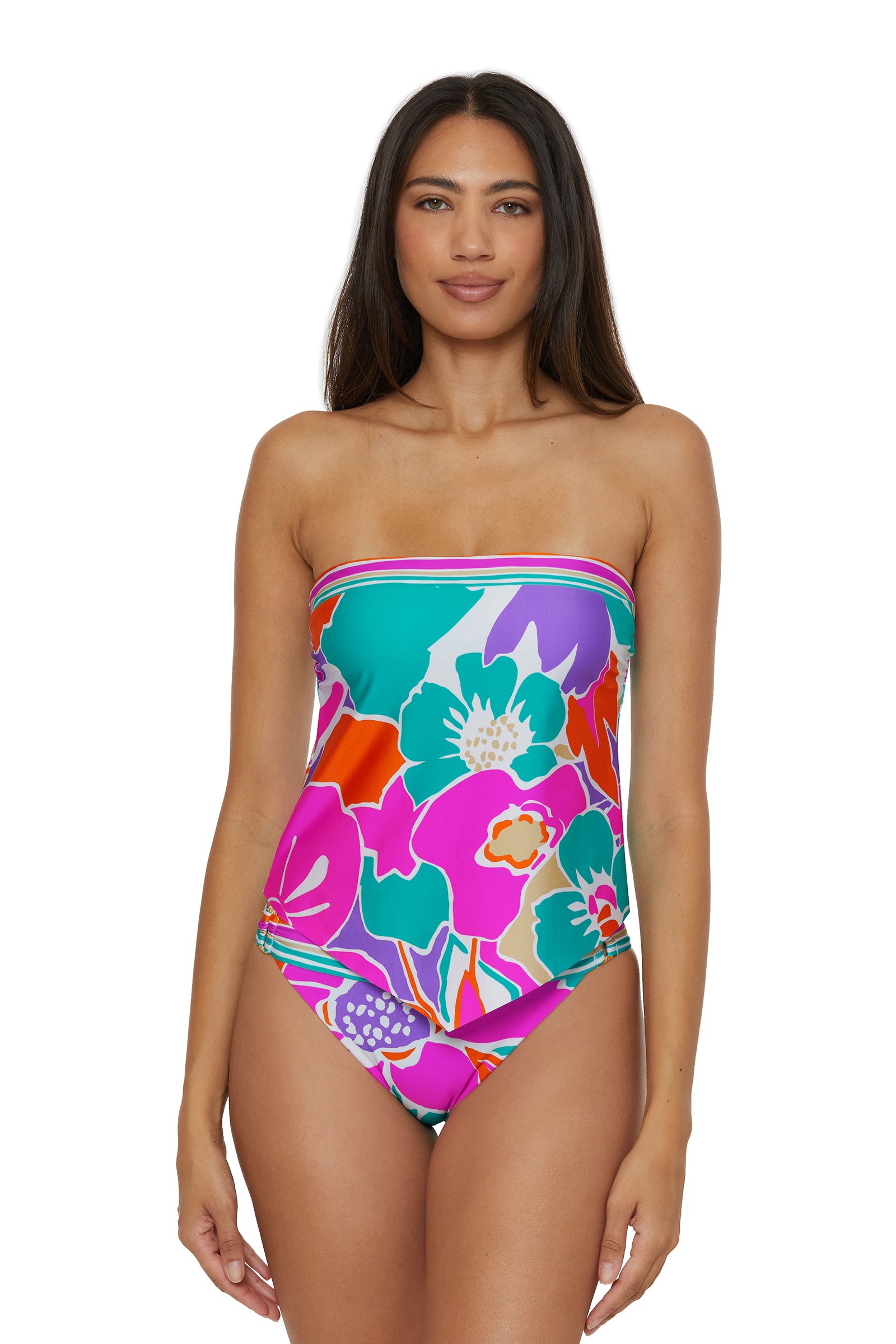 A woman with long dark hair models the TRINA TURK SWIM Handkerchief Tankini Swim Top - Amalfi, a colorful floral-patterned tankini in pink, orange, teal, purple, and white, standing against a white background.