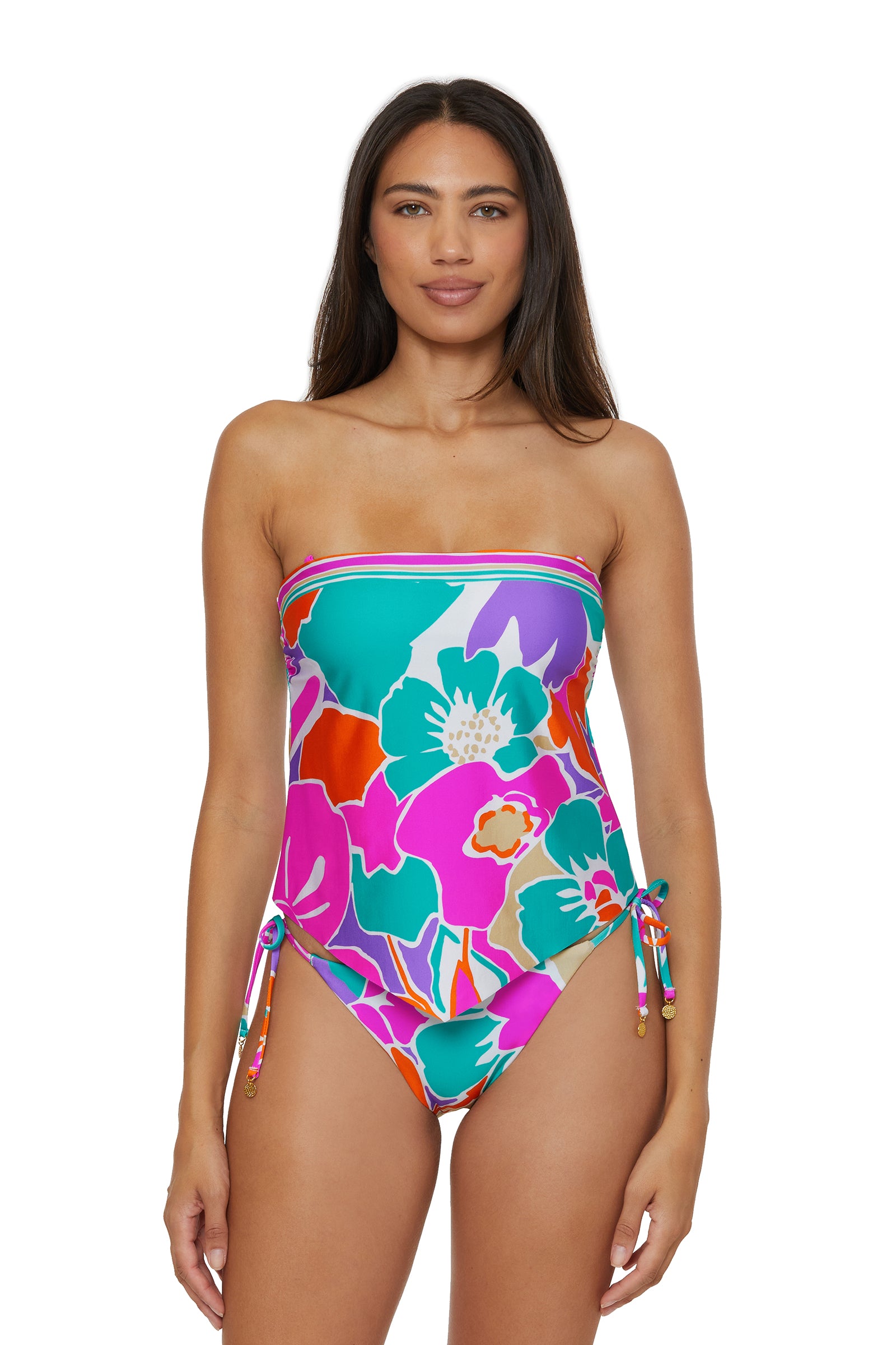 A woman with long brown hair wears the TRINA TURK SWIM Handkerchief Tankini Swim Top - Amalfi, featuring a bold floral pattern in pink, teal, green, and orange. She stands against a white background.